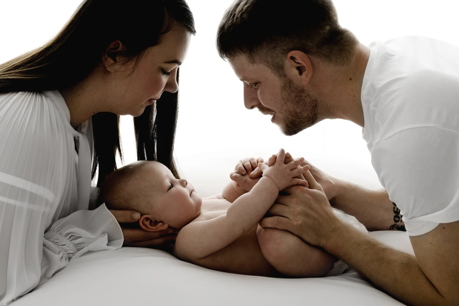 Mum and dad looking down at their 9 month old baby during relaxed studio photoshoot in Dundee