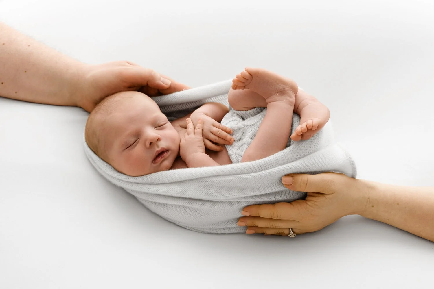 Wrapped newborn baby with parents hands at Mabel and Moose studio Dundee