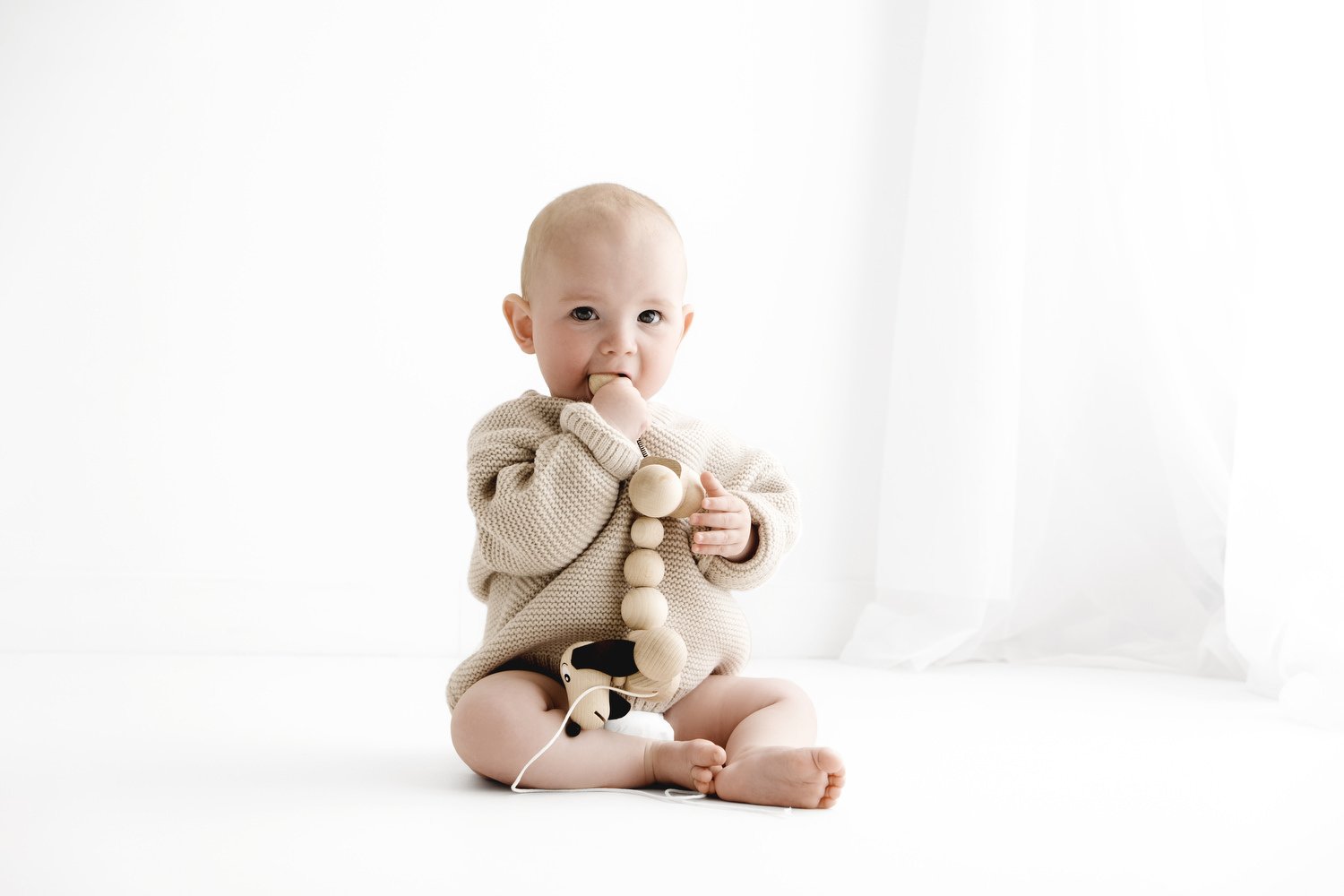 7 month baby sitting playing with wooden toy in natural knitted jumper