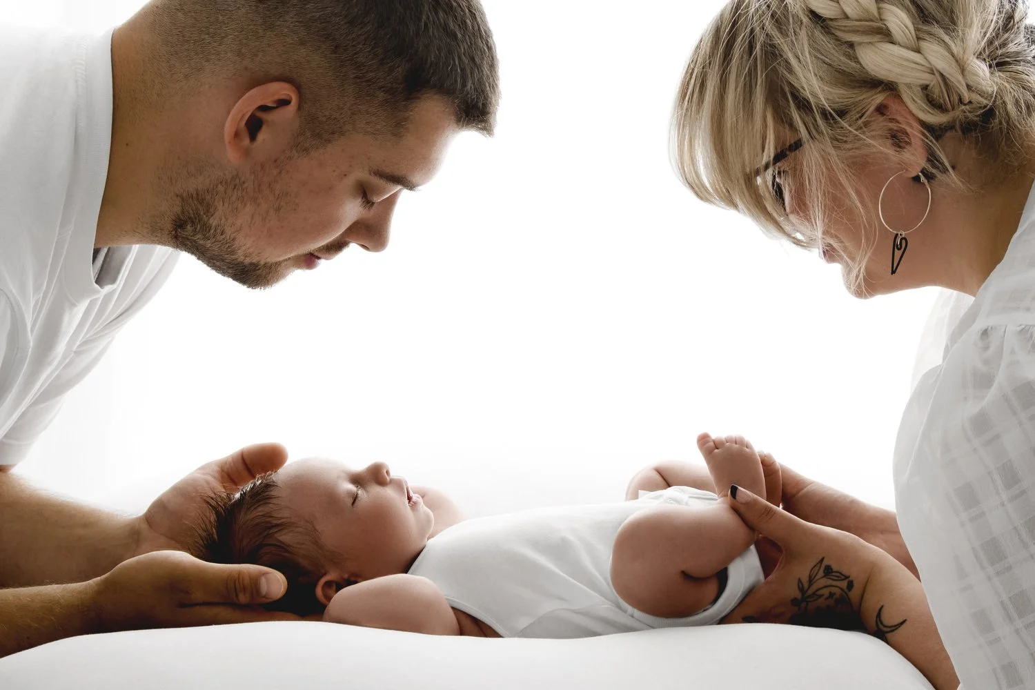 Mum and dad looking down at their newborn baby in natural studio portrait