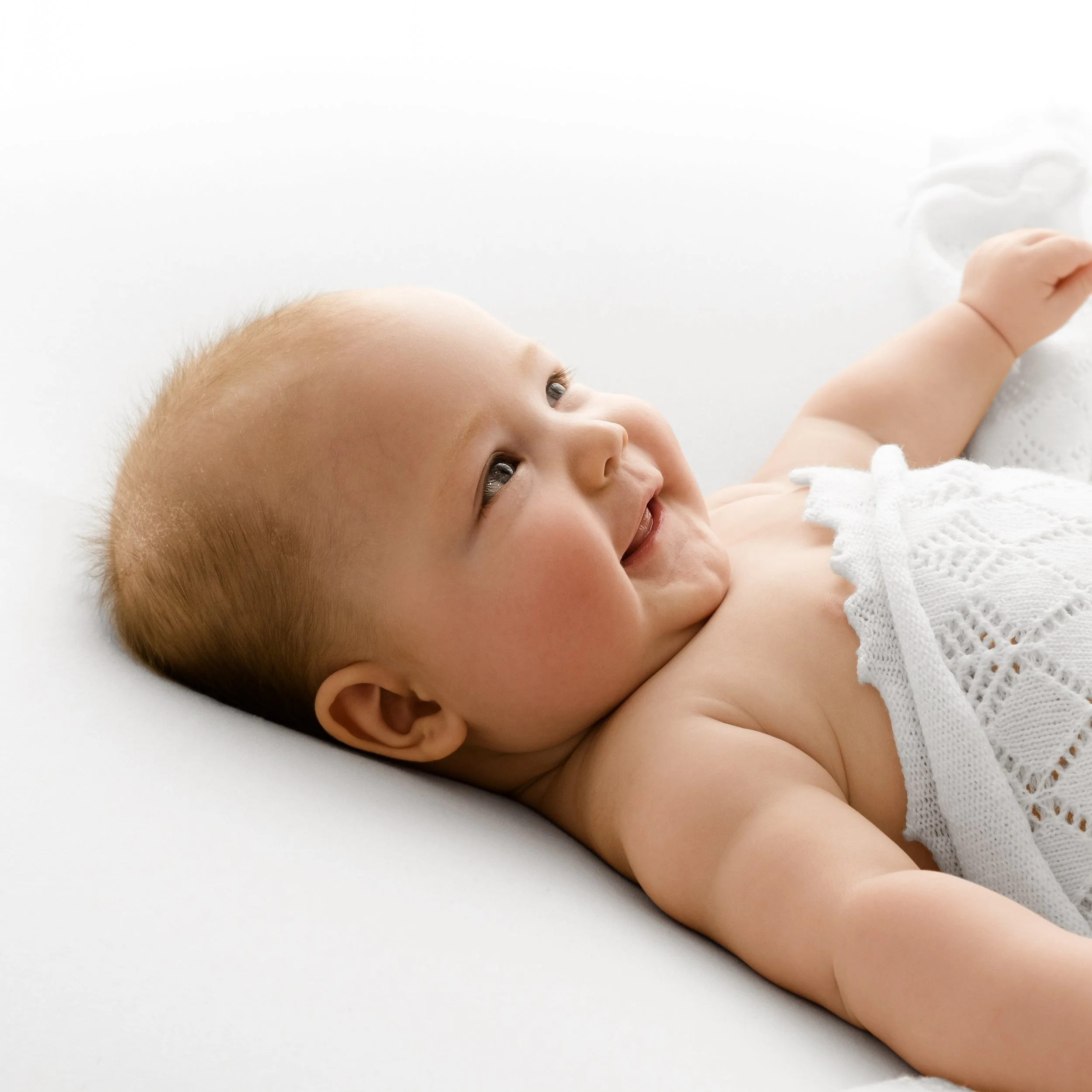 baby lying on back under a white blanket in a photo session in dundee