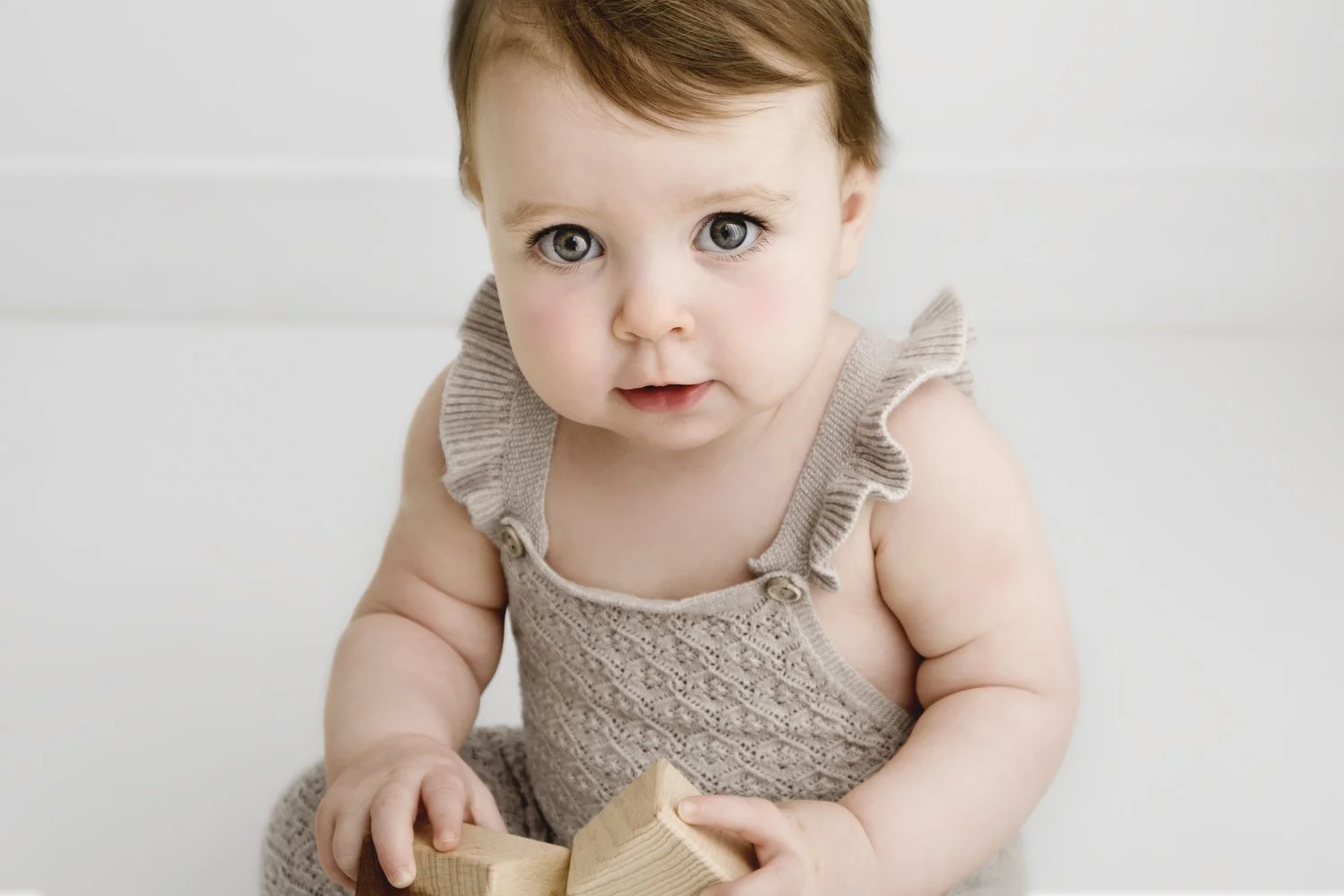 9 month old baby girl looking at camera wearing neutral knitted romper