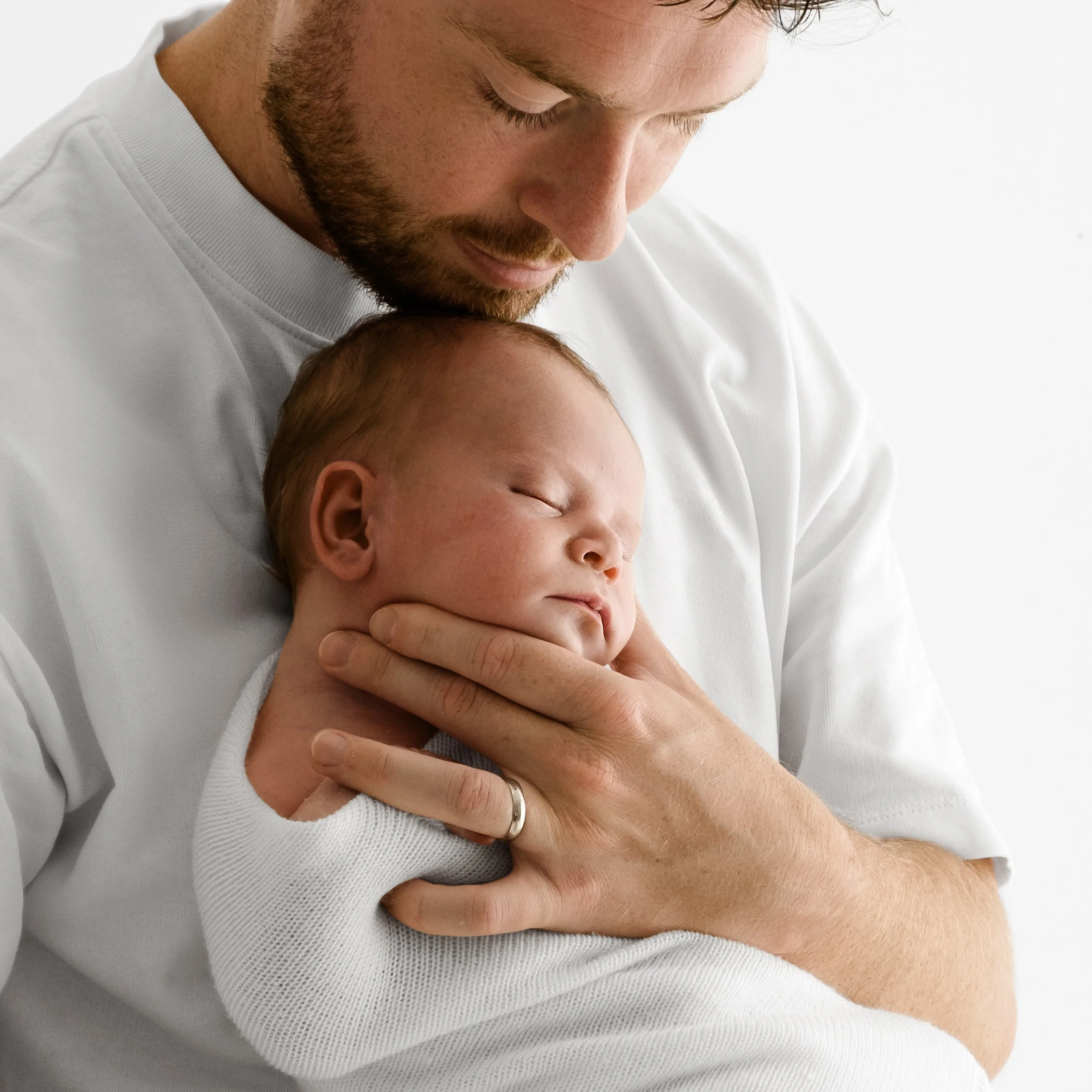 Dad in white t-shirt holding newborn wrapped in white blanket at Dundee studio