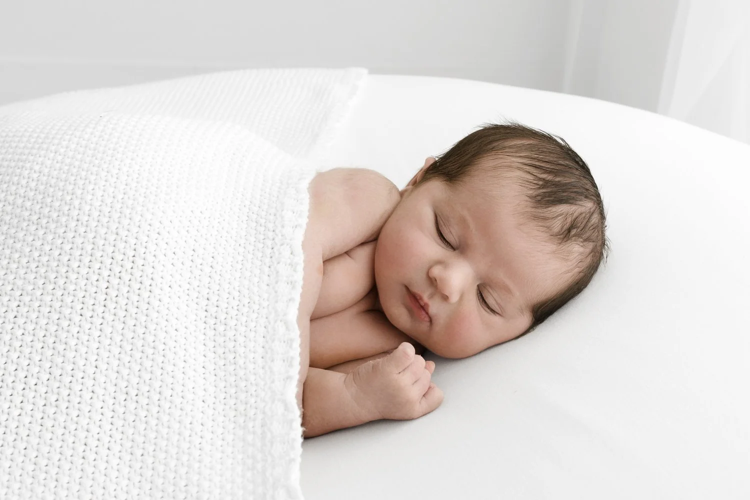 Sleeping newborn baby lying on side wrapped in white shawl at Mabel and Møøse newborn photography studio Dundee
