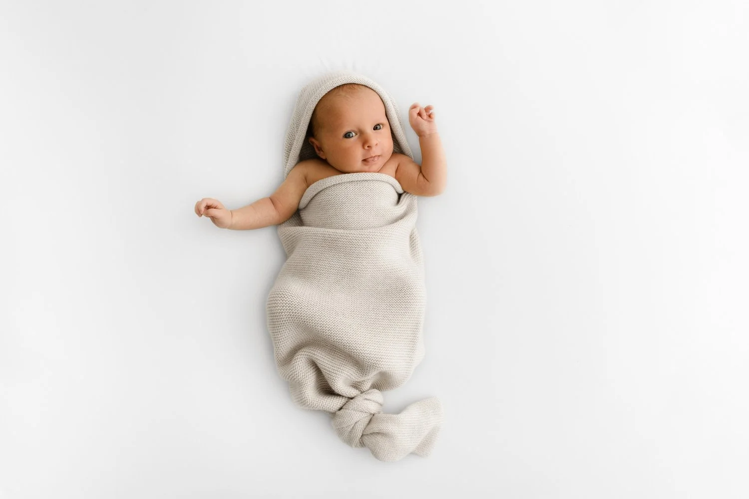 newborn baby comfortably lying awake in a swedish-style knitted cocoon wrap