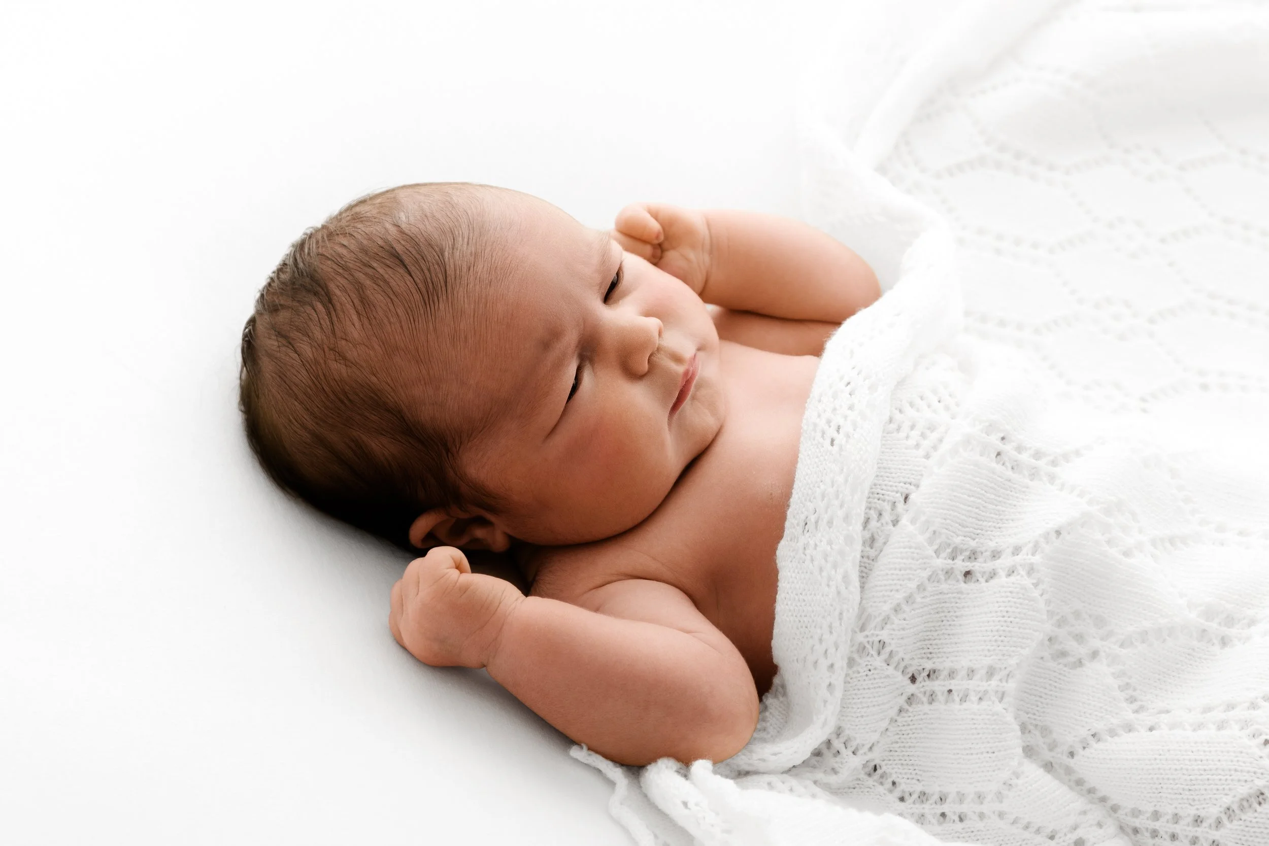 Newborn lying on side under white shawl during natural Dundee studio photoshoot