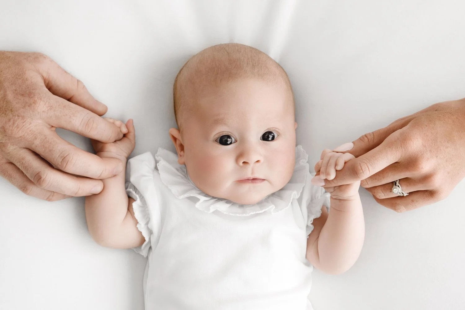 baby holding parents hands in White baby bodysuit with Peter Pan collar for newborn photoshoot at Mabel and Moose Dundee