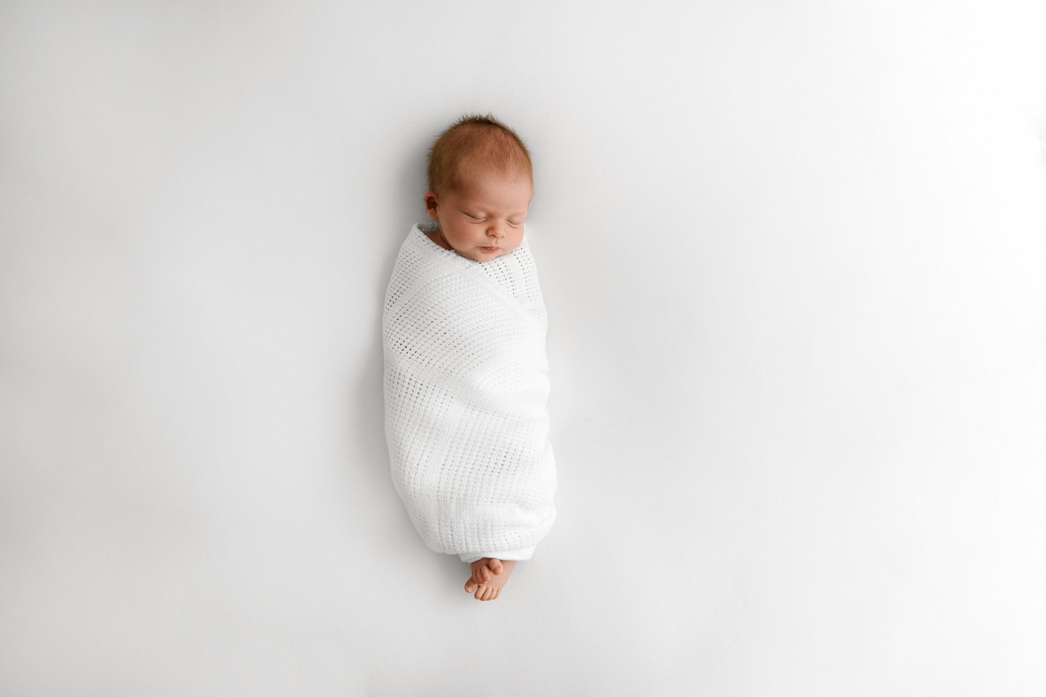 sleeping newborn baby wrapped in a very natrual style in a white cellular blanket