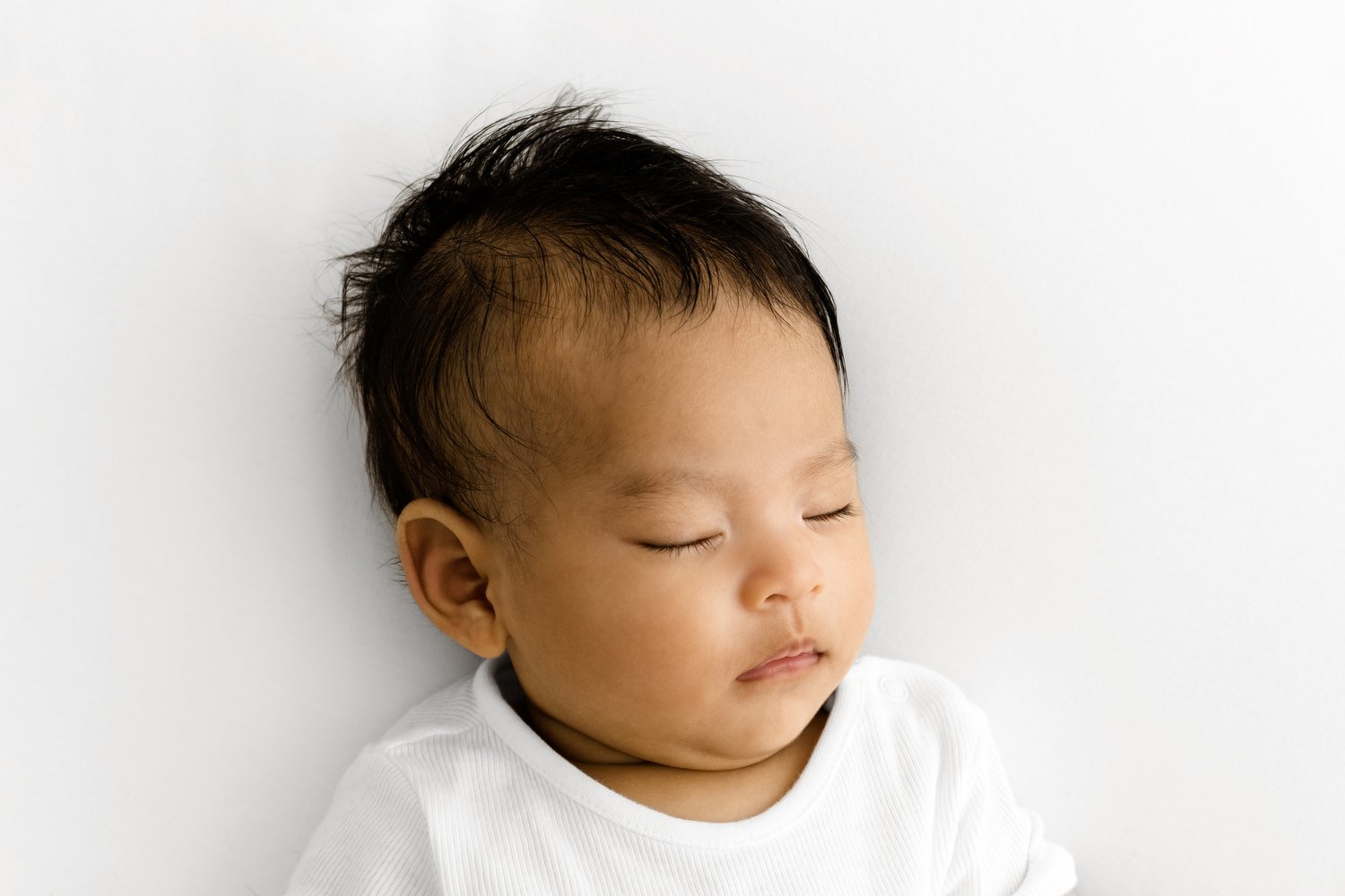 Three month old baby sleeping  in white vest during studio photoshoot