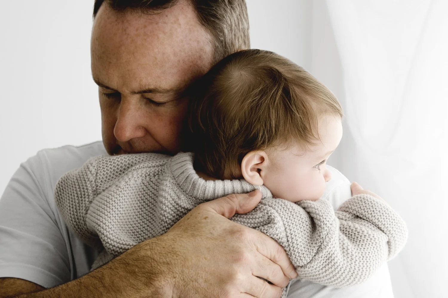 dad hugging 9 month old baby who wears a knitted neutral jumper