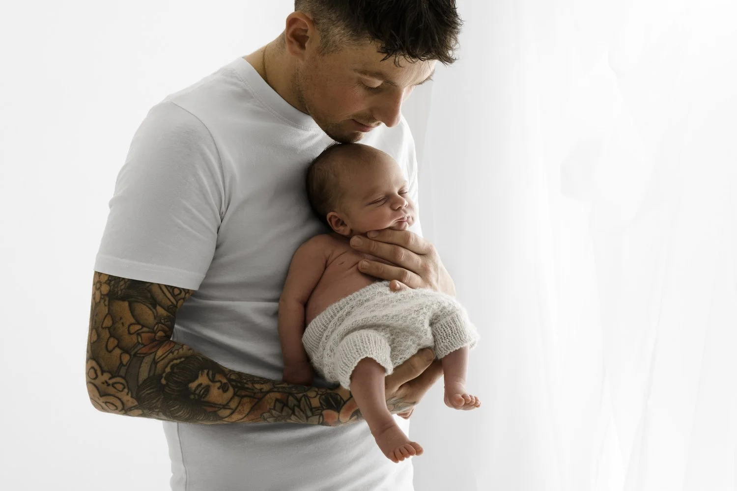 Dad with tattoos holding his newborn baby at Mabel and Møøse newborn photography studio Dundee