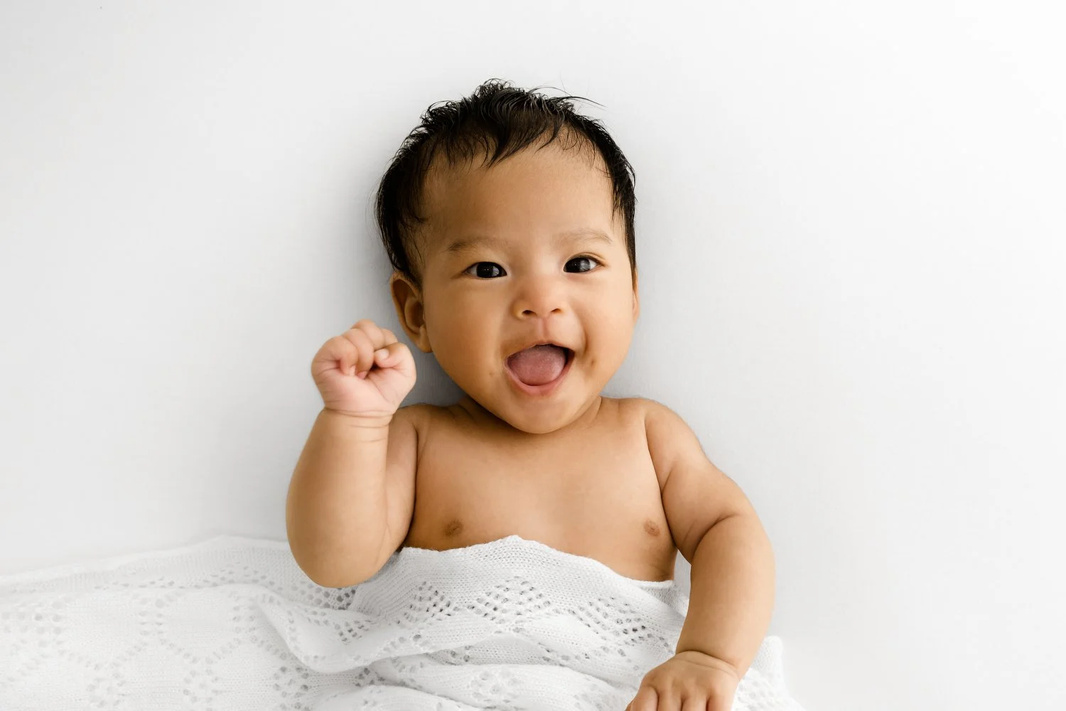100 day old baby smiling under a white lace shawl
