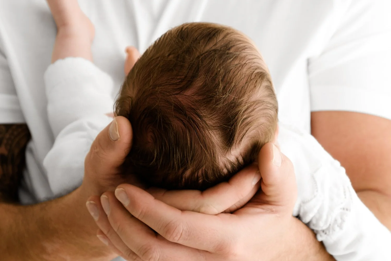 Newborn baby’s head gently held in father’s hands during studio photoshoot