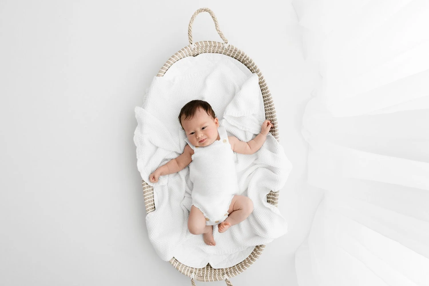 Awake 3 week old newborn in Moses basket wearing white knitted outfit in Dundee studio