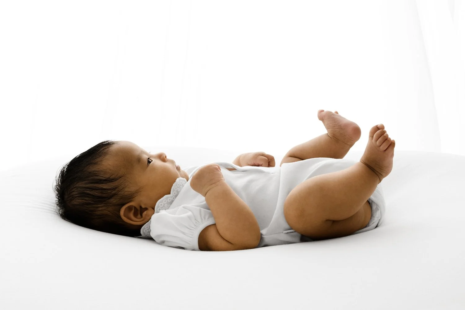 Three month old baby lying on her side wearing a white vest in natural light studio in Dundee