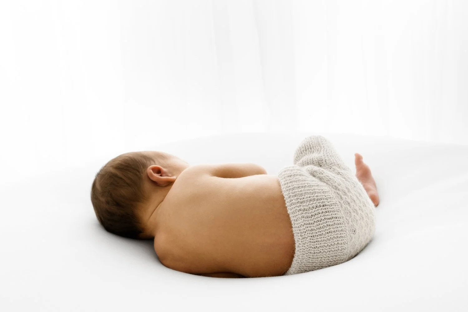 beautiful simple image of a baby's back. newborn is wearing natural hand knitted bloomers