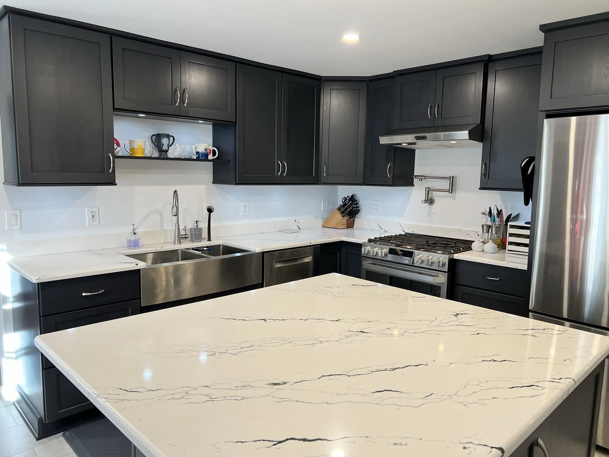 Kitchen photo showing large island in foreground, stainless appliances and black cabinets.