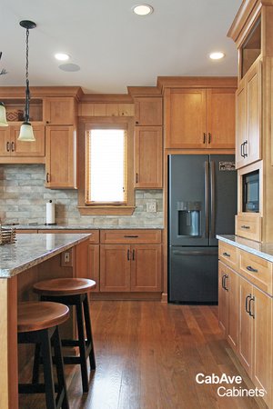 Modern kitchen with wooden cabinets, stainless steel refrigerator, stone backsplash, and bar stools at a kitchen island.