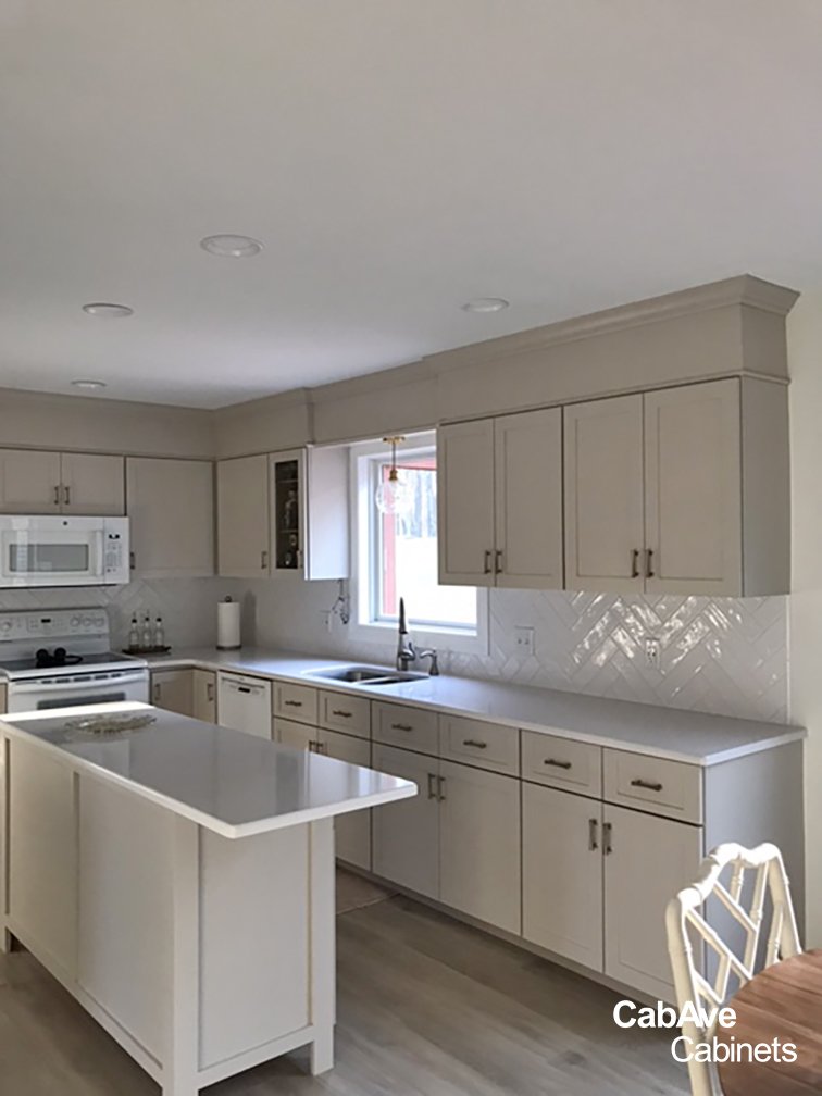 Modern kitchen with white cabinets, island, and appliances, featuring a herringbone tile backsplash.
