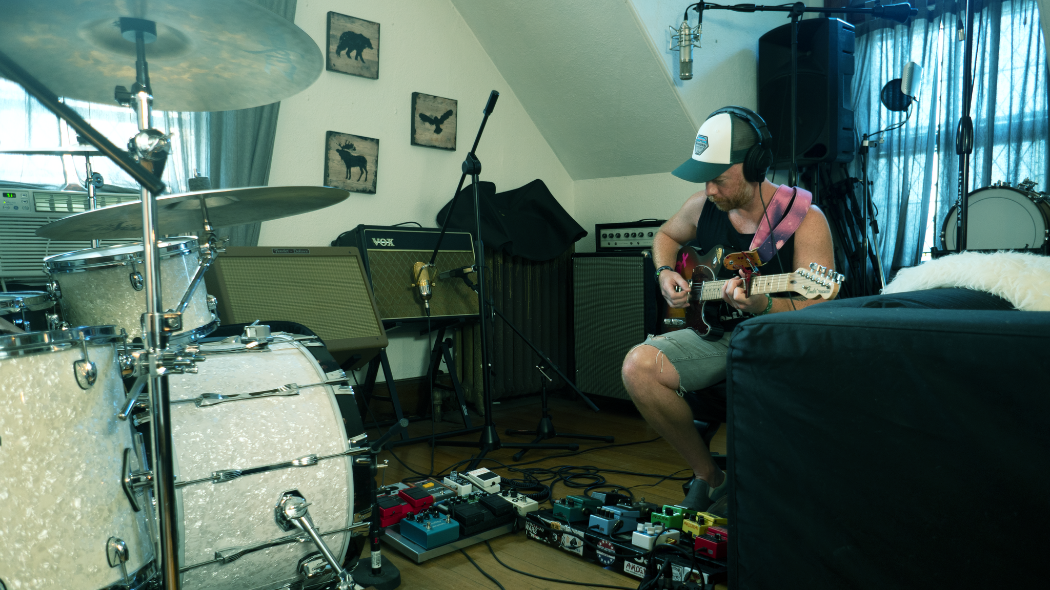 Musician playing electric guitar in room with drum set and audio equipment.