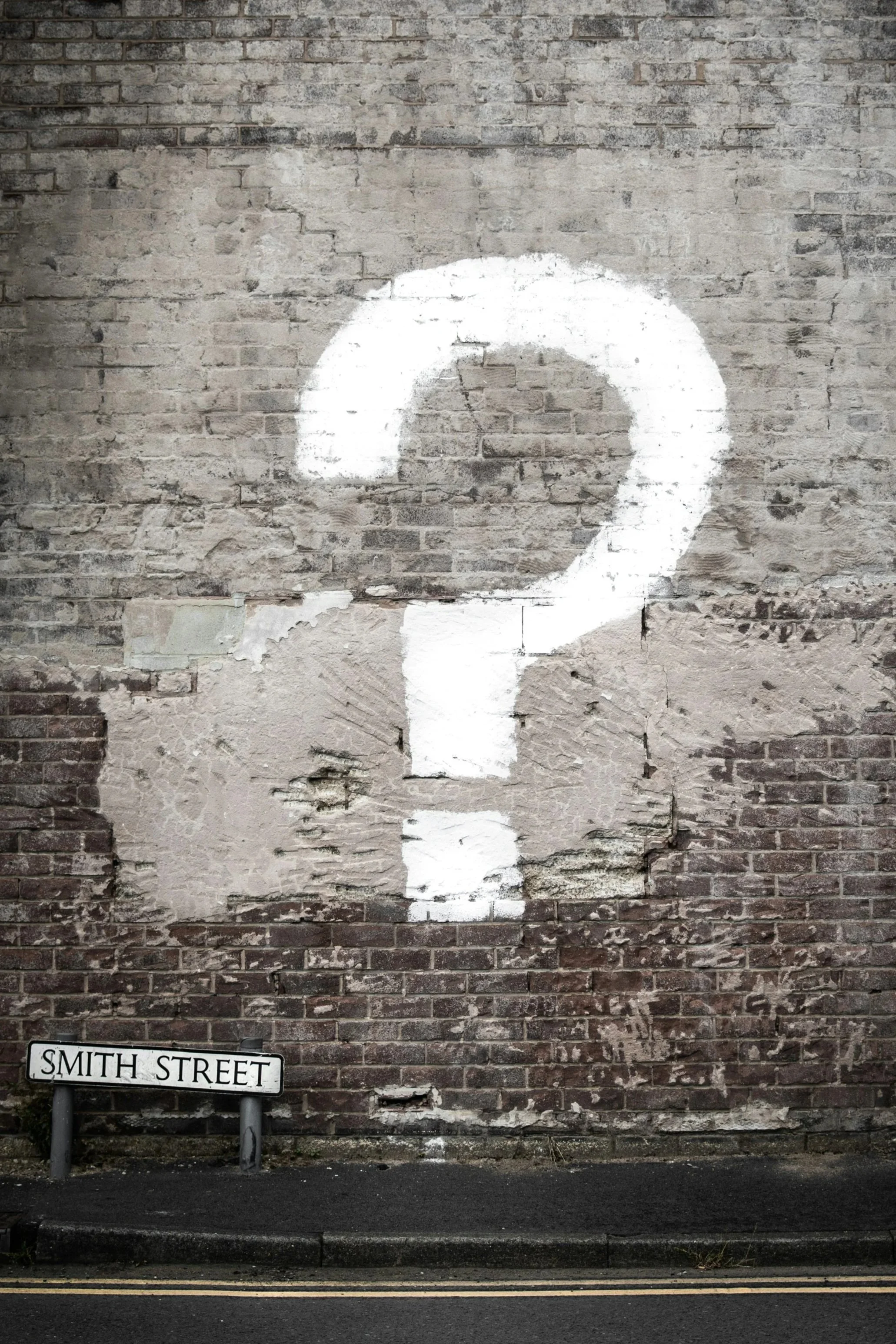 black and white brick wall with a big white question mark painted on it