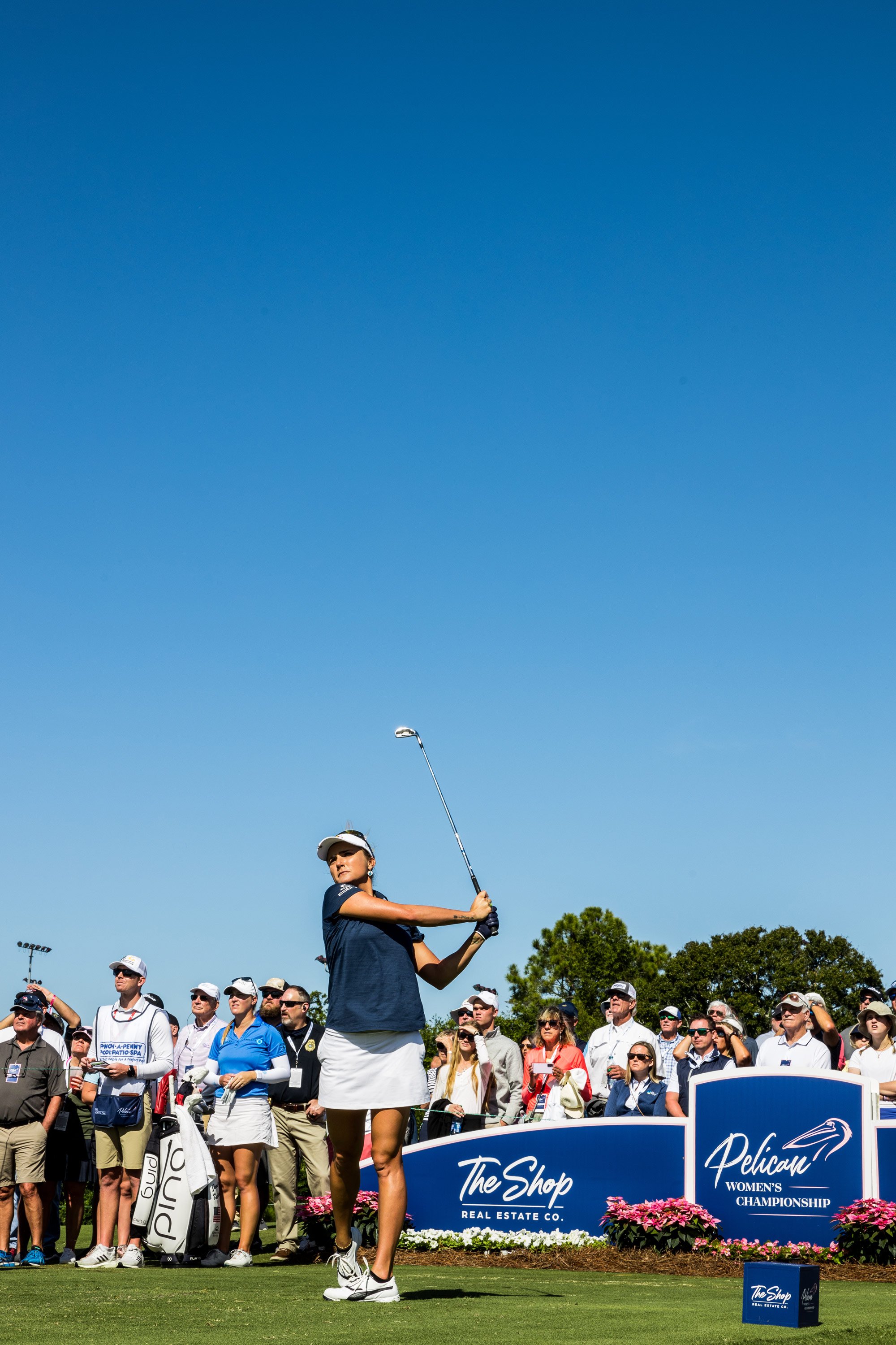  Female golf athlete making stoke during golf tournament in front of a group of spectators. 