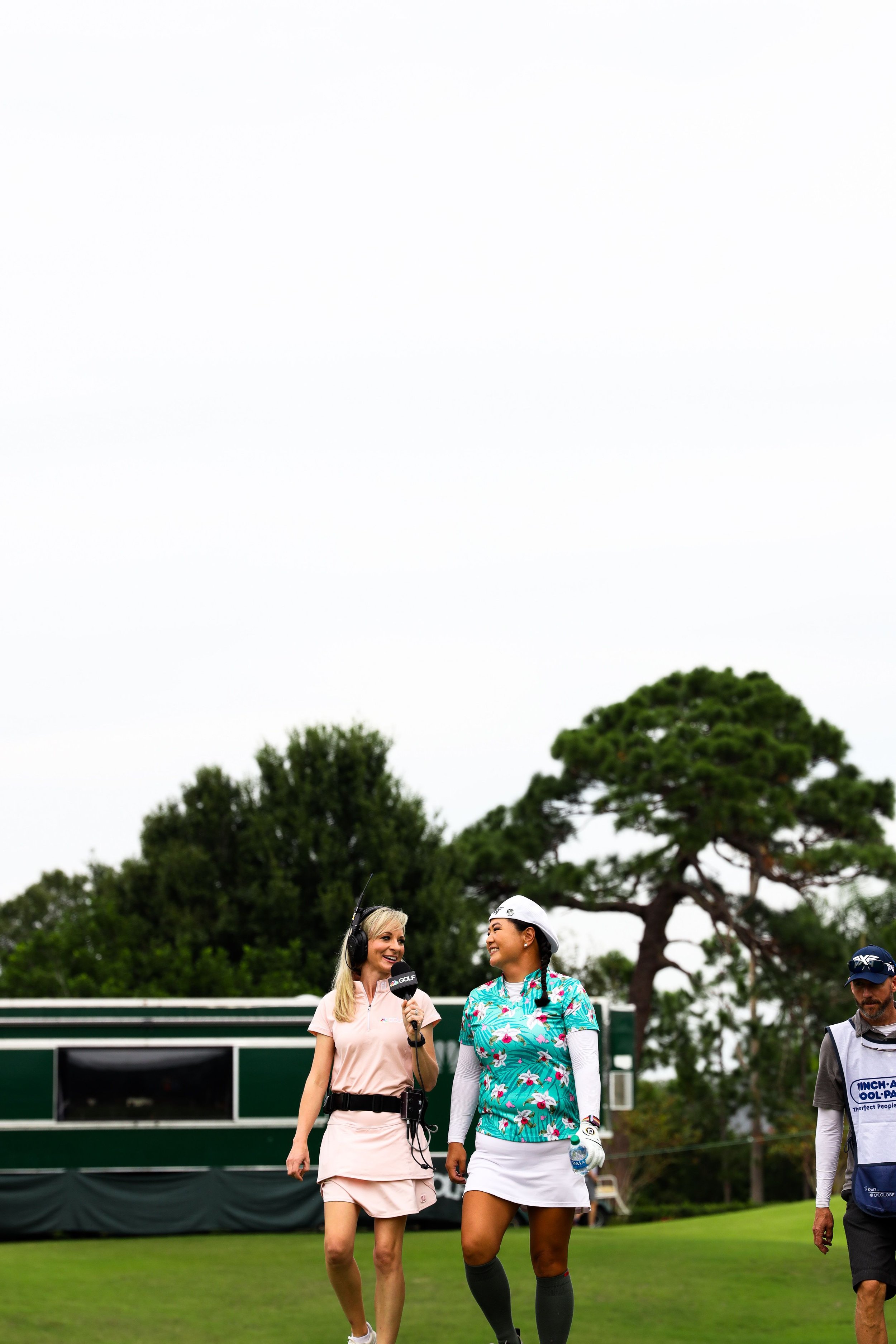  Female golf athlete smiling and walking while being interviewed by journalist. 