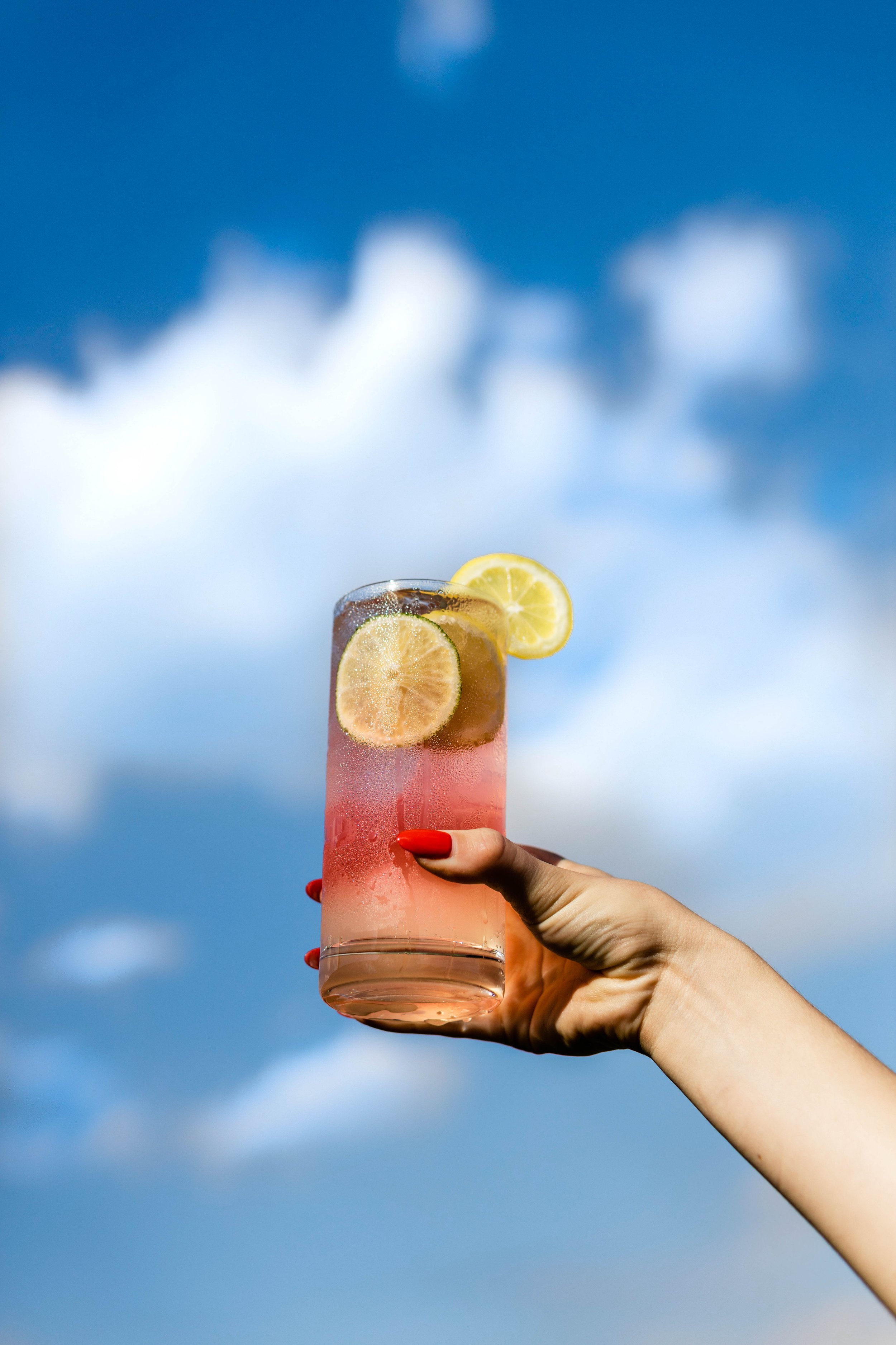  Fruity drink held up to the cloudy blue sky. 