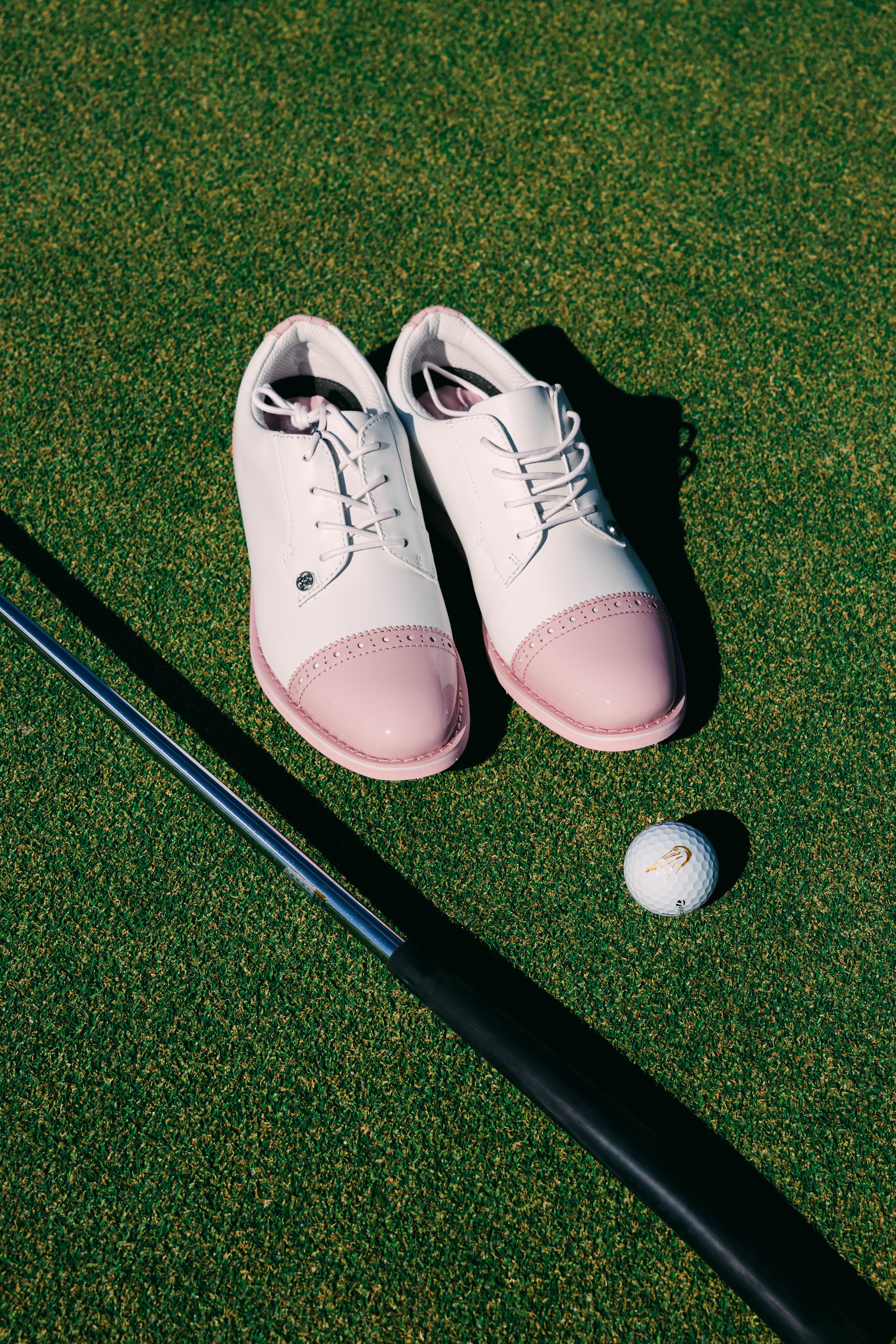  Pink and white golf shoes next to a club and golf ball. 