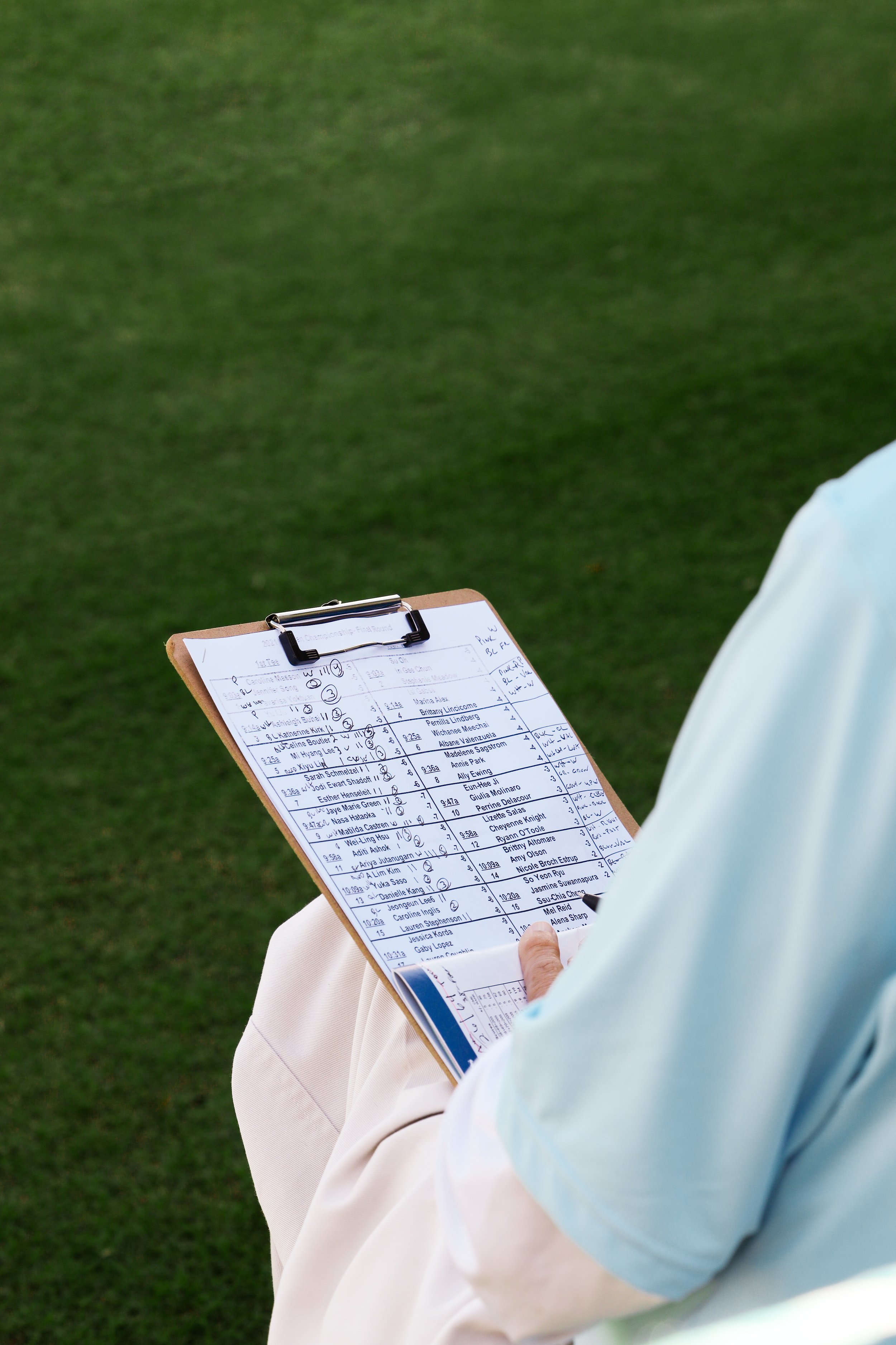  Person holding clipboard of score and athlete lineup for golf tournament. 
