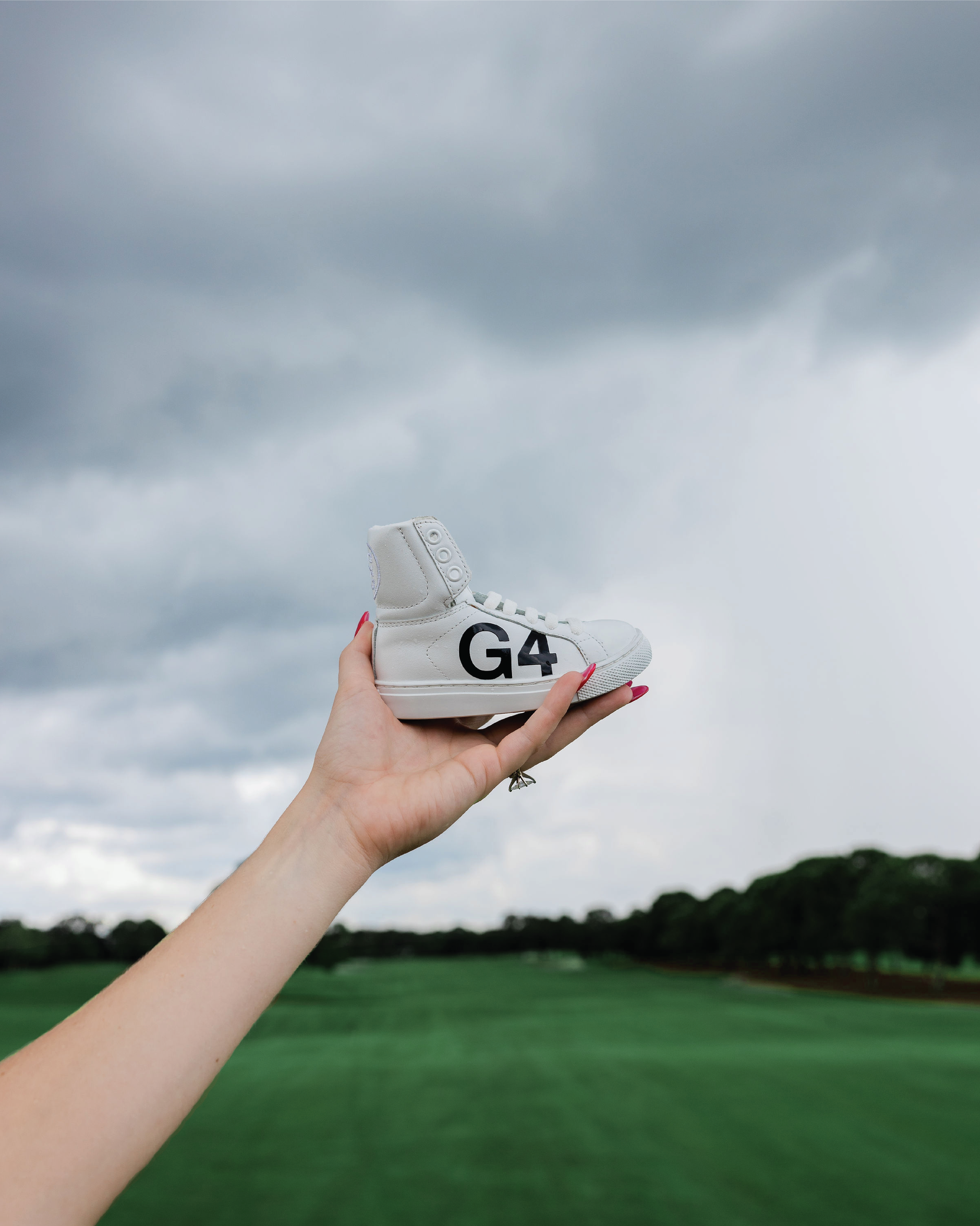  Baby shoe with “G4” text held up against sky. 