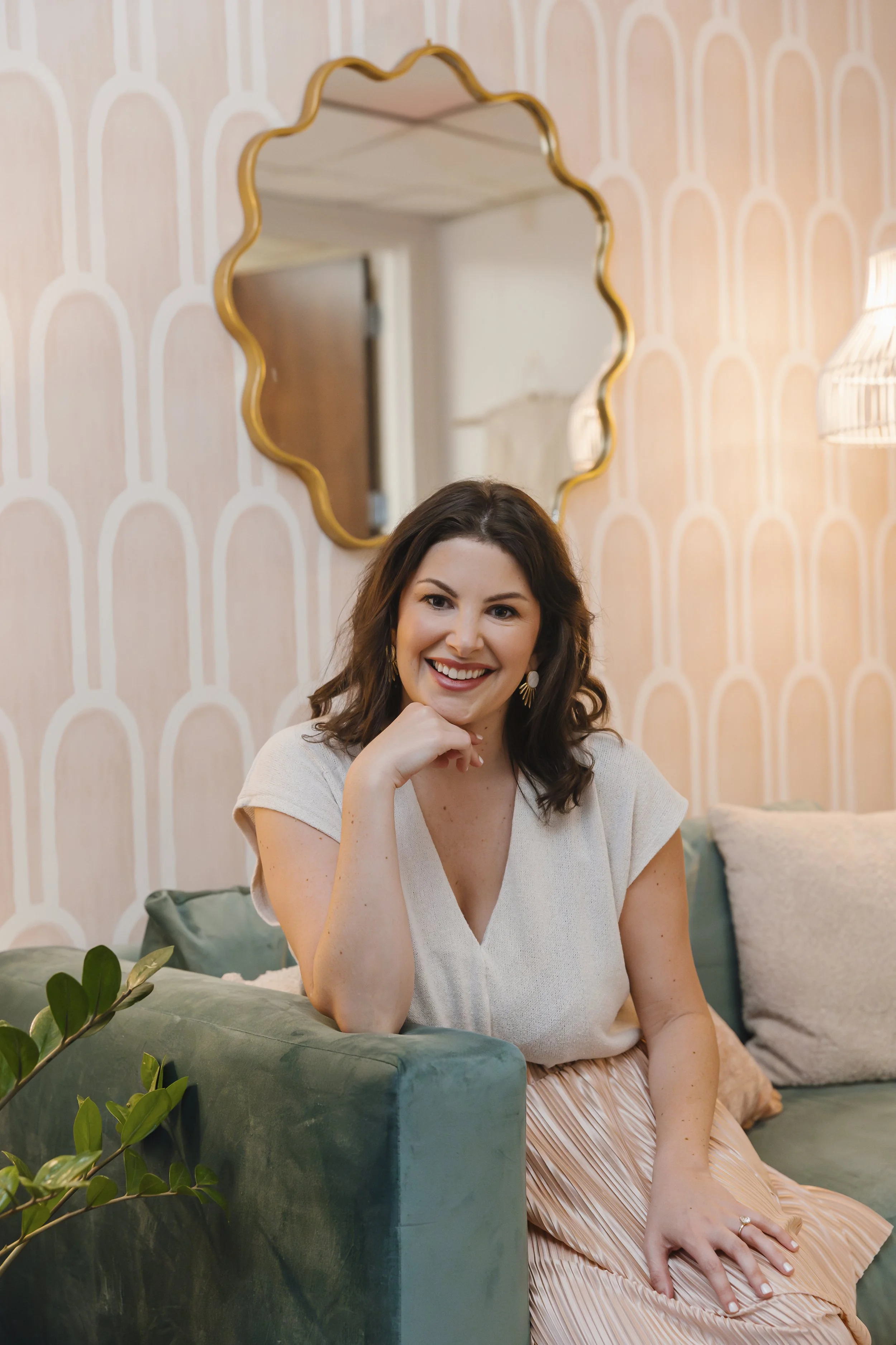 A woman sitting on a green sofa, smiling, with her hand resting on her chin.