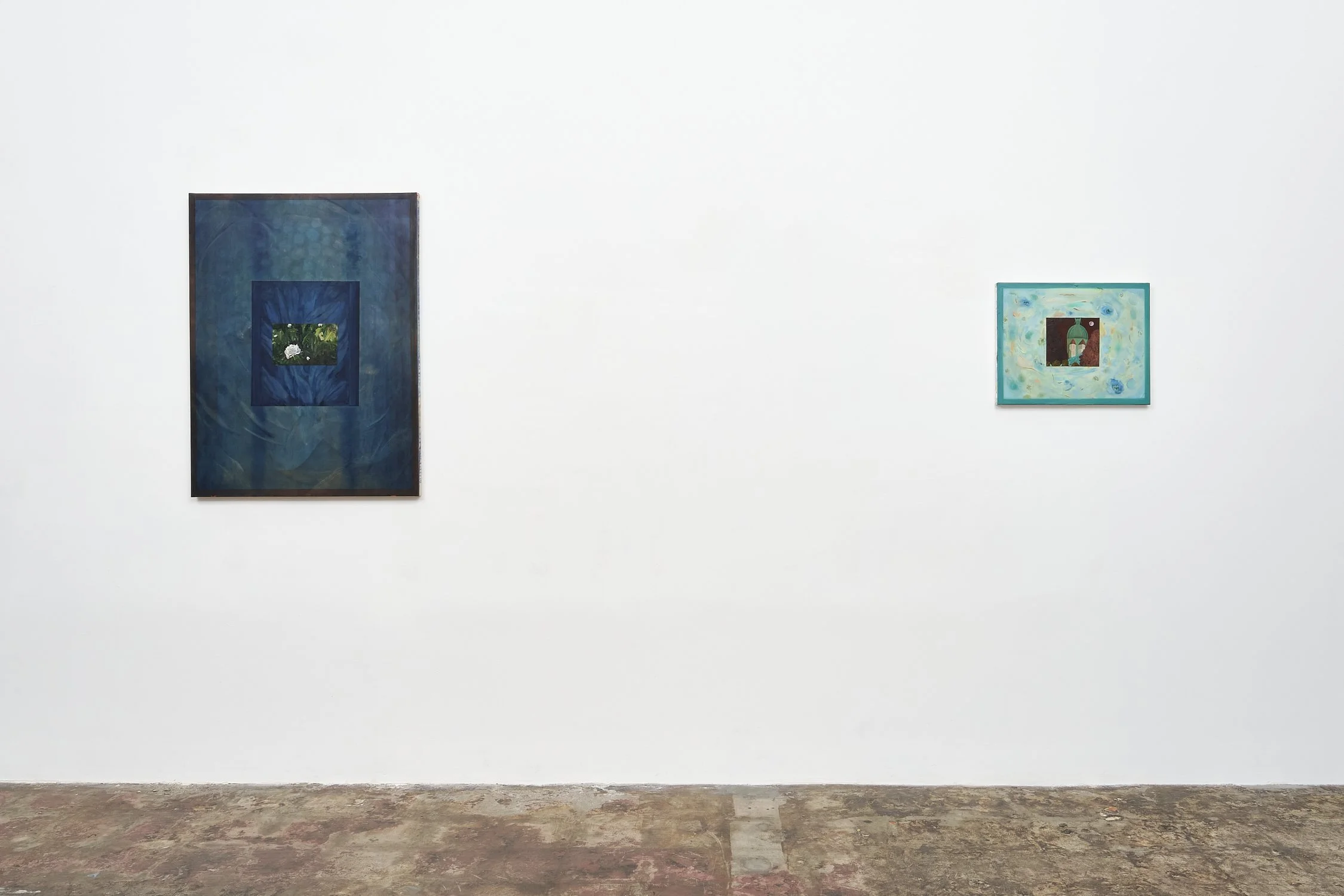 Two framed artworks displayed on a white gallery wall, with a concrete floor visible below.