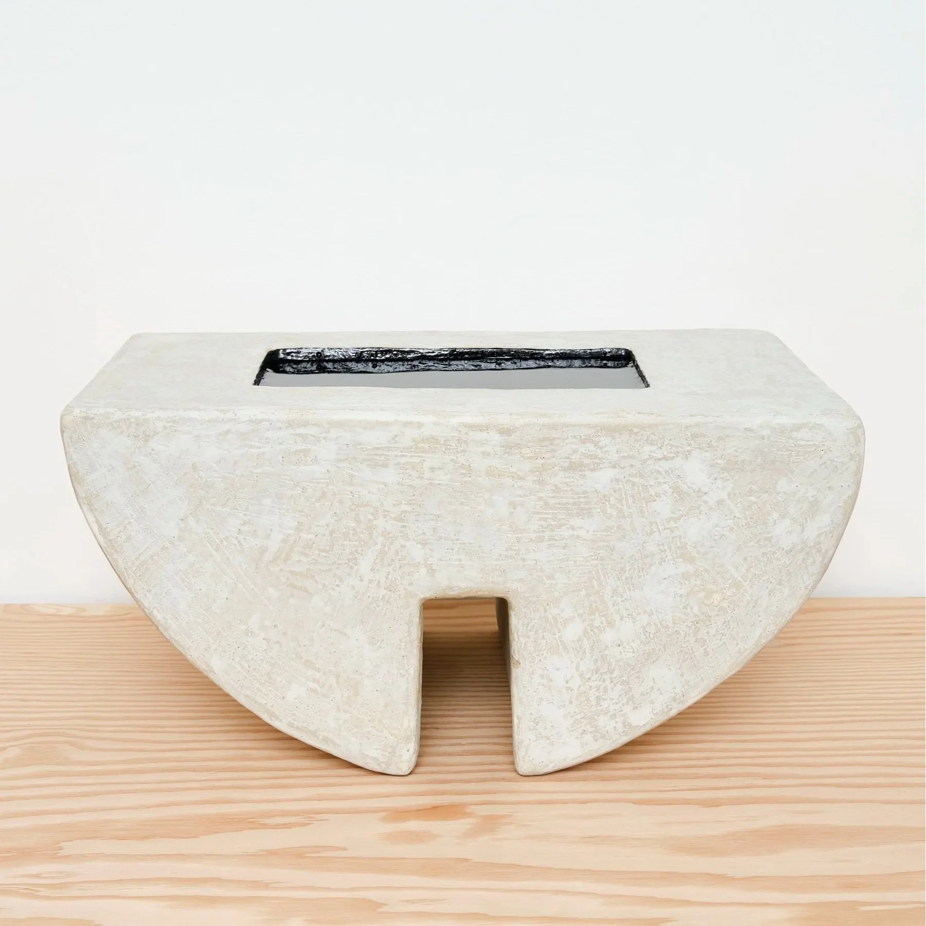 Minimalist rectangular stone sculpture with a black inset on top, placed on a light wooden surface against a white wall.