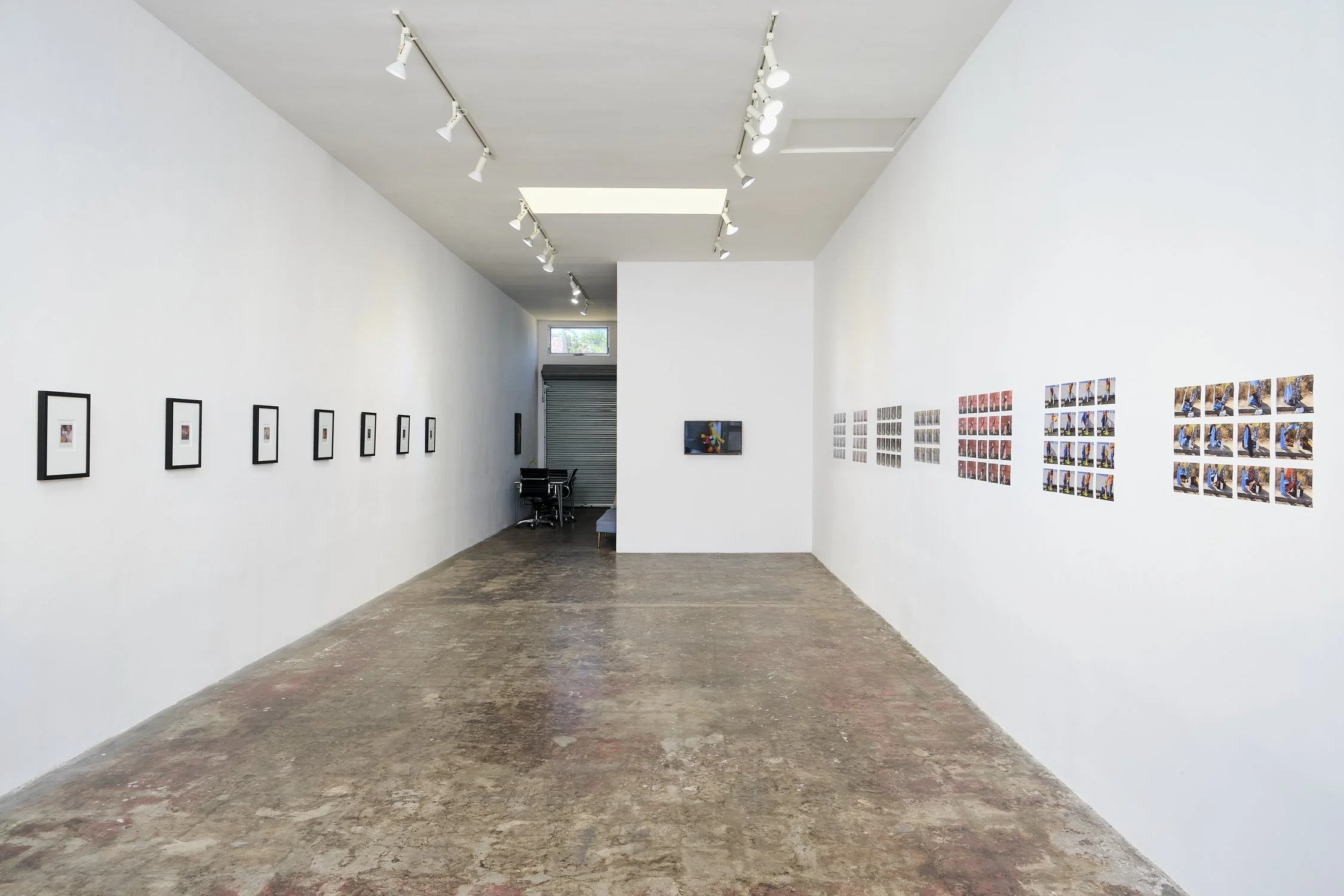 An art gallery with white walls displaying framed photographs and colorful artwork, with track lighting on the ceiling illuminating the pieces.