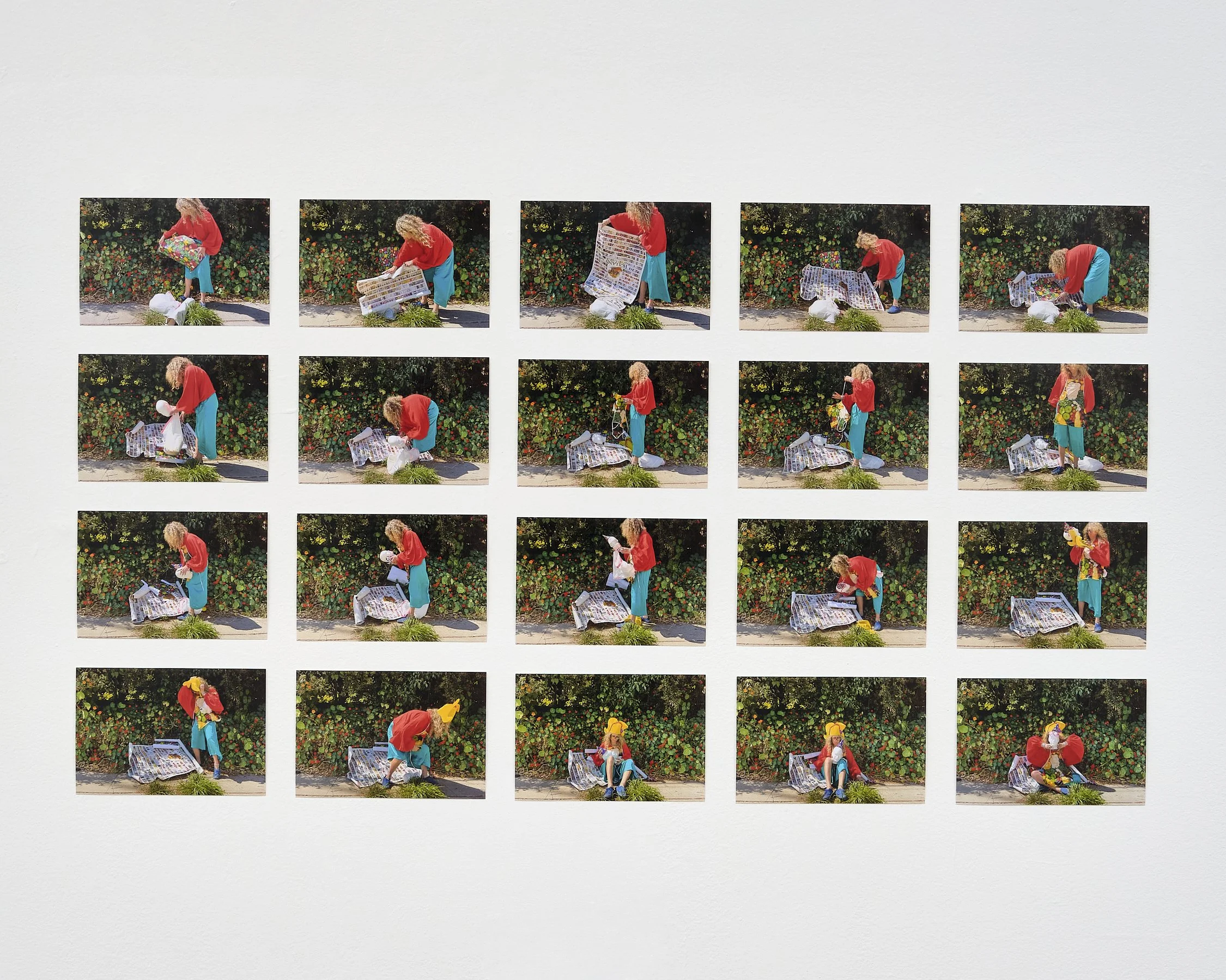 A person in a red shirt and blue pants is seen in multiple frames opening and handling a colorful gift bag, displaying various steps of unwrapping the gift, with a backdrop of green bushy plants with red flowers.