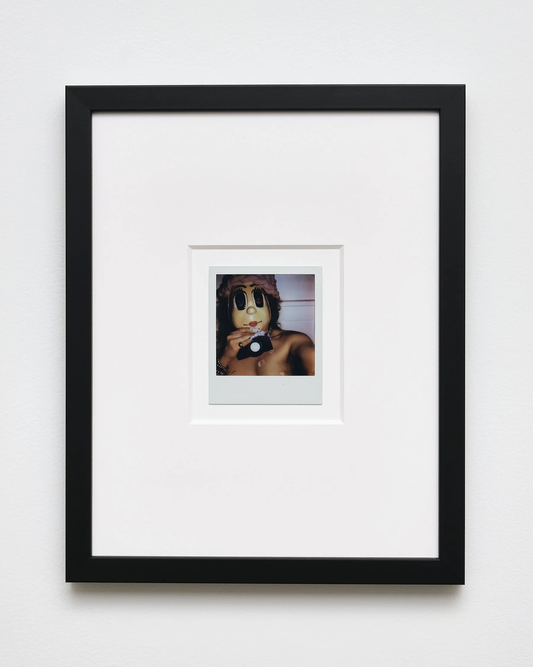 Framed photograph of a person wearing a mask resembling a cartoon character, holding a camera and appearing to take a photo of herself.