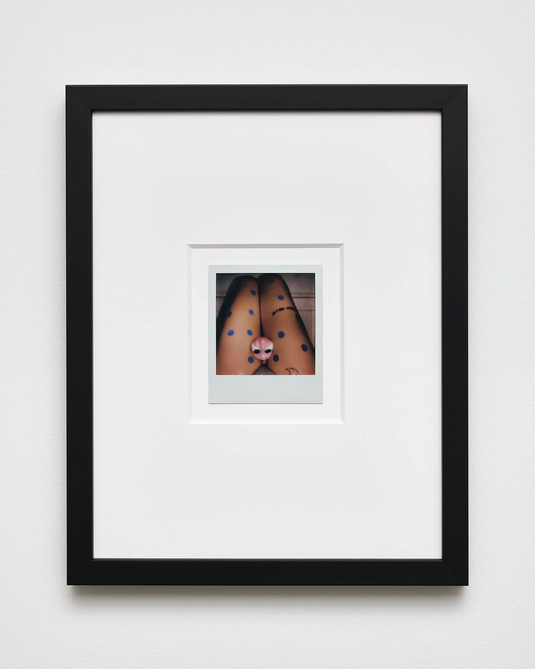 Multiple white picture frames nested inside each other on a white wall, with the innermost frame containing a photo of feet with cartoonish animal face socks and fishnet stockings.