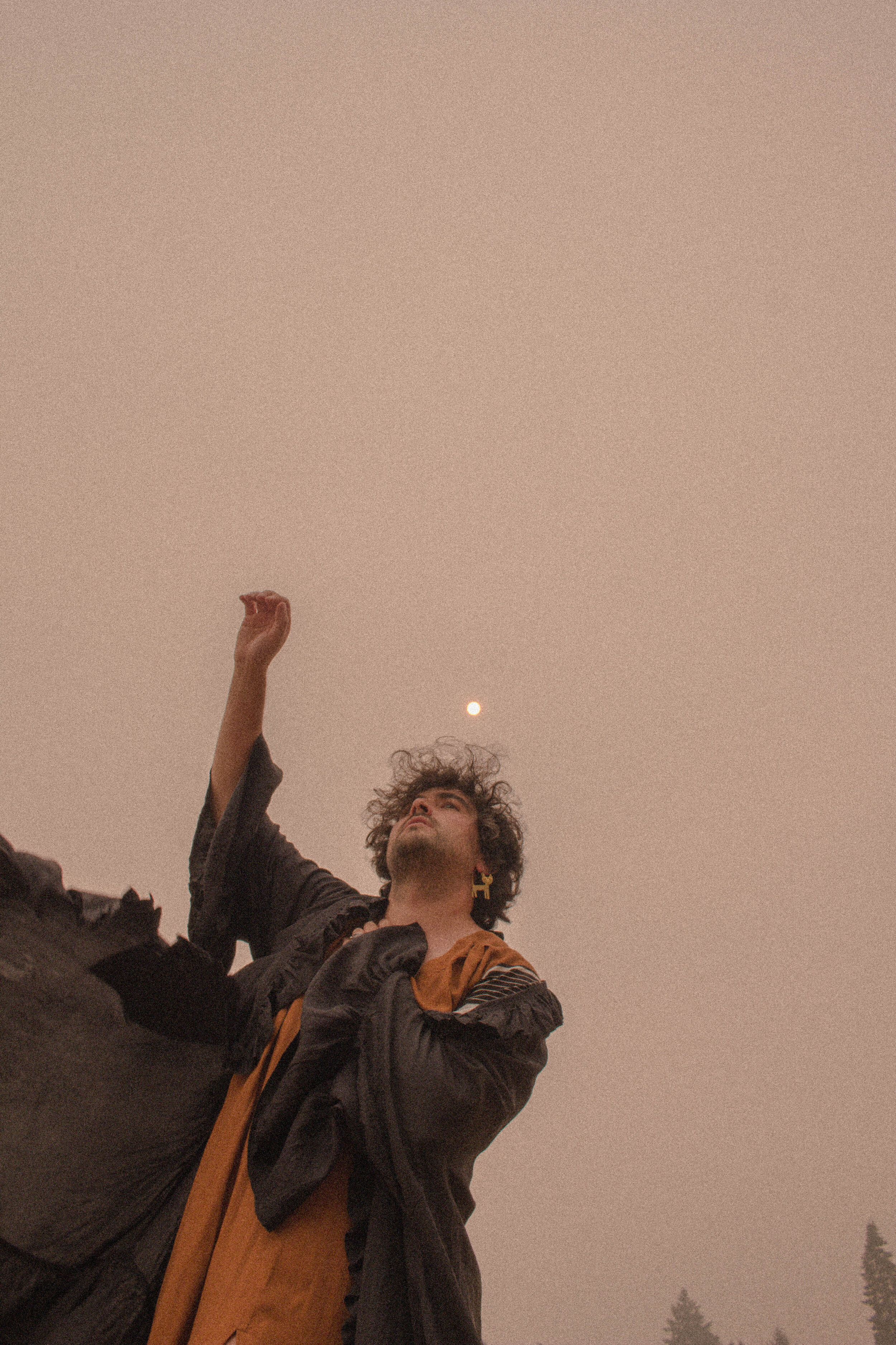 A person with curly hair is raising their hand with the sky and a bright moon in the background.