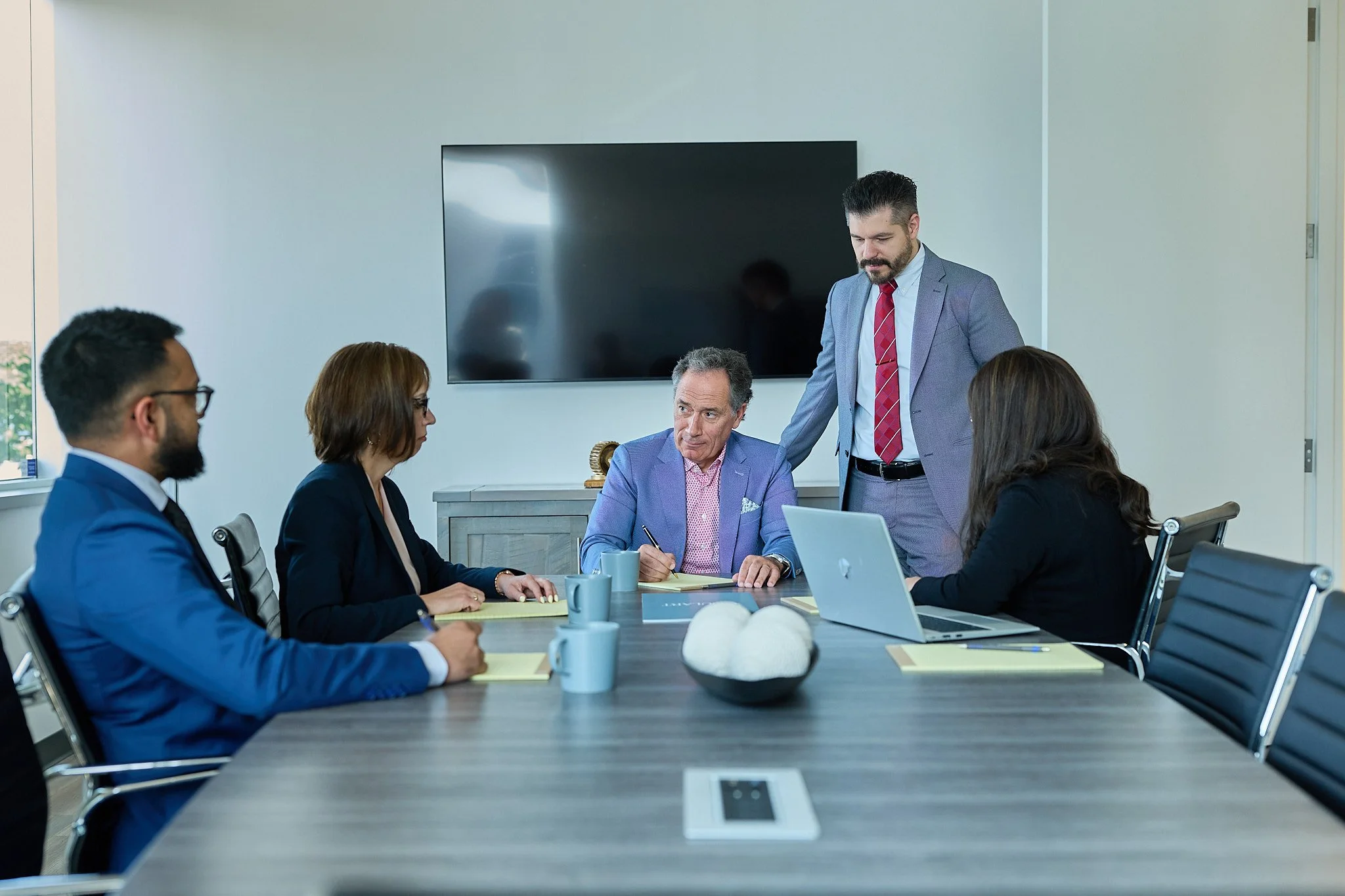 Business meeting with six professionals around a conference table in a modern office, engaged in discussion.