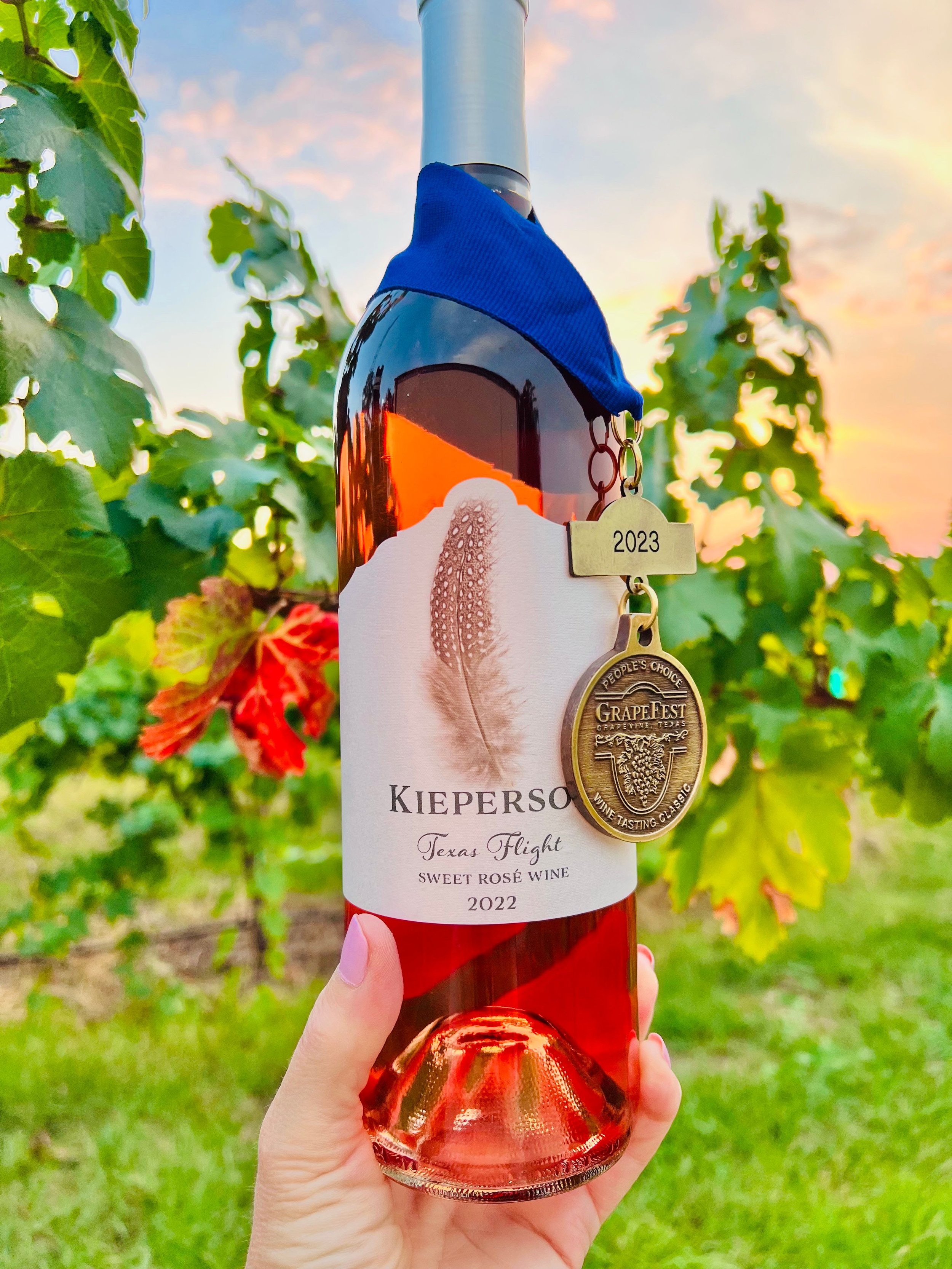 Bottle of Kiepersol Texas Flight Sweet Rosé Wine 2022 with a medal, held in front of grapevines.