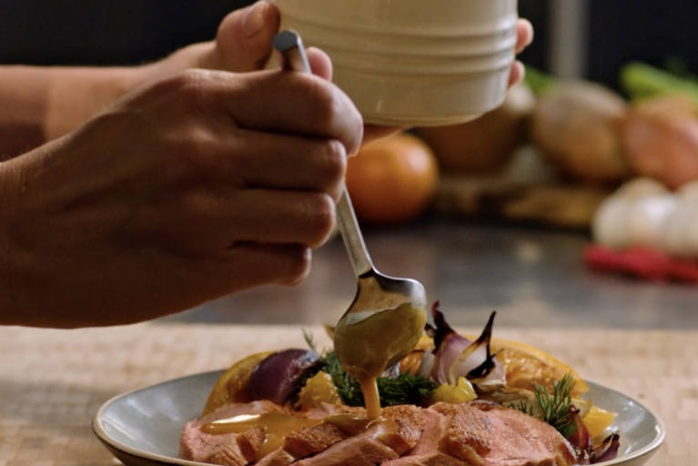 A person pouring gravy over a plate of food with onions, herbs, and vegetables.