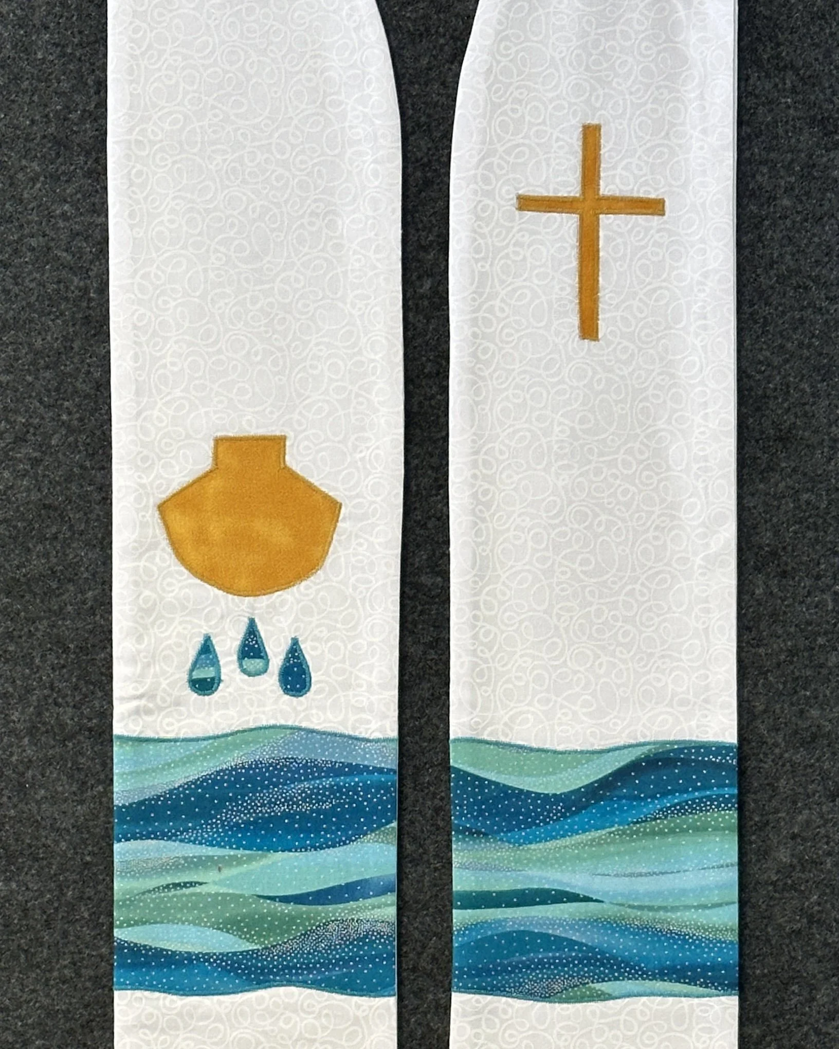 Detail of a white stole for baptism with a shell, three water droplets and flowing water.
