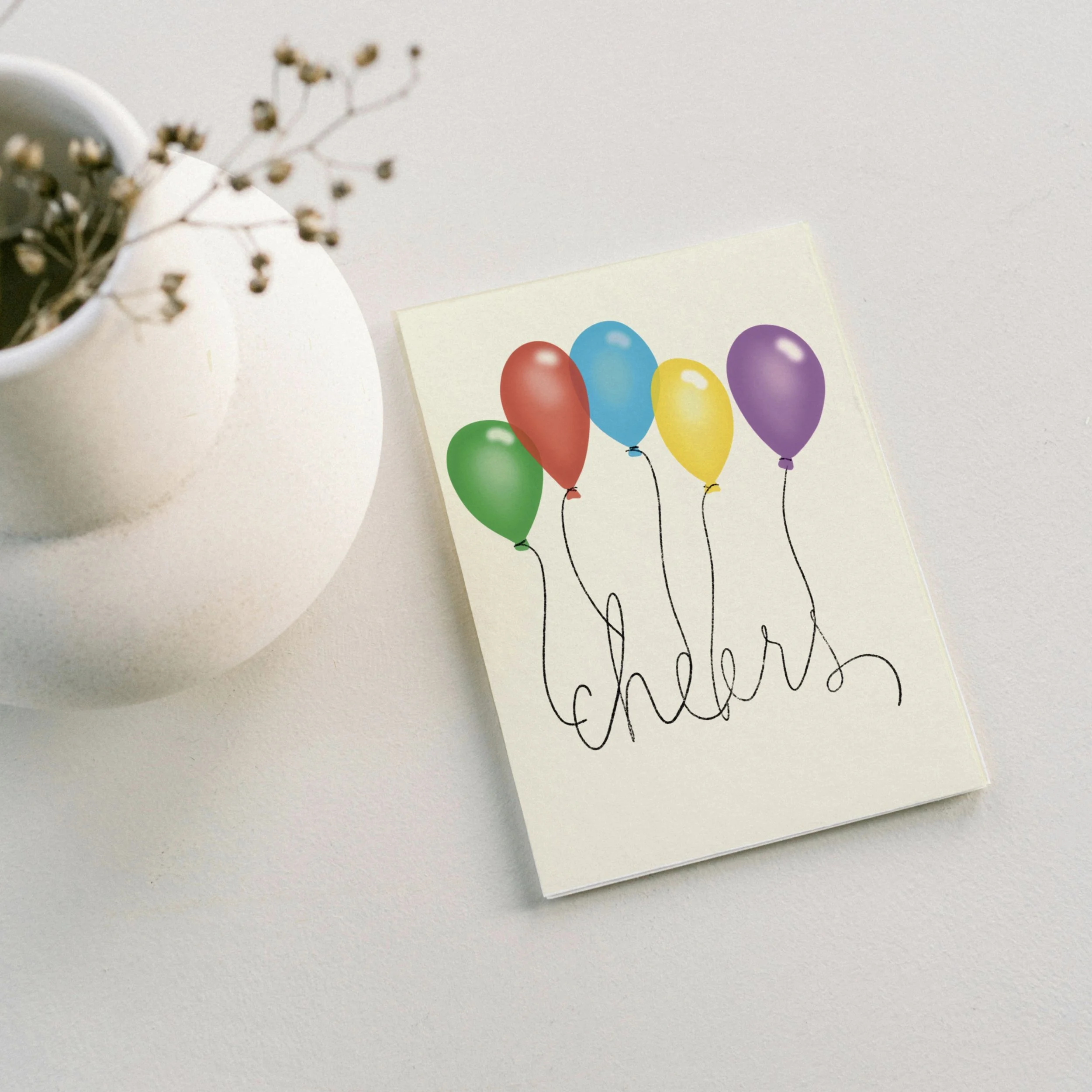 The word cheers held up by festive balloons on teh front of a card by Carrot Top Studio shown with a coordinating envelope and a vase of flowers