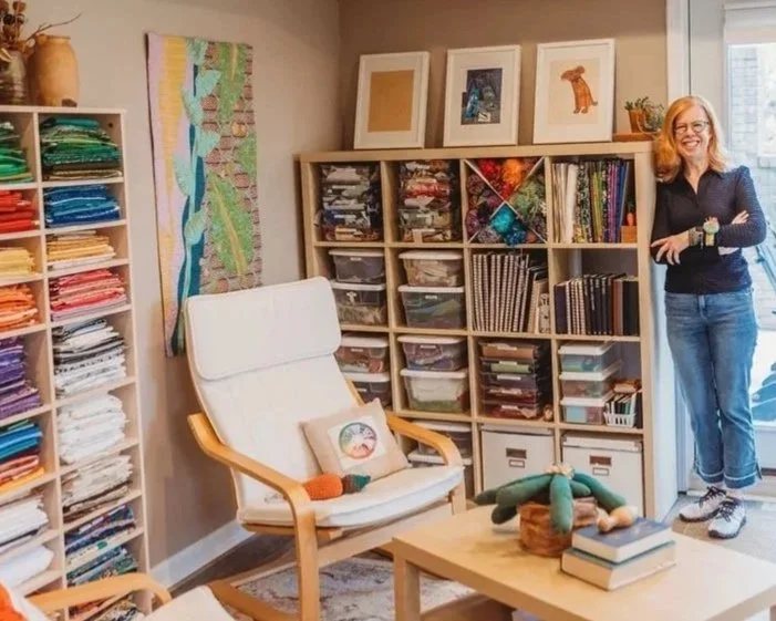 Artist Jenny Gallo in her studio surrounded by fabric and other supplies for creating clergy stoles and faith based gifts.