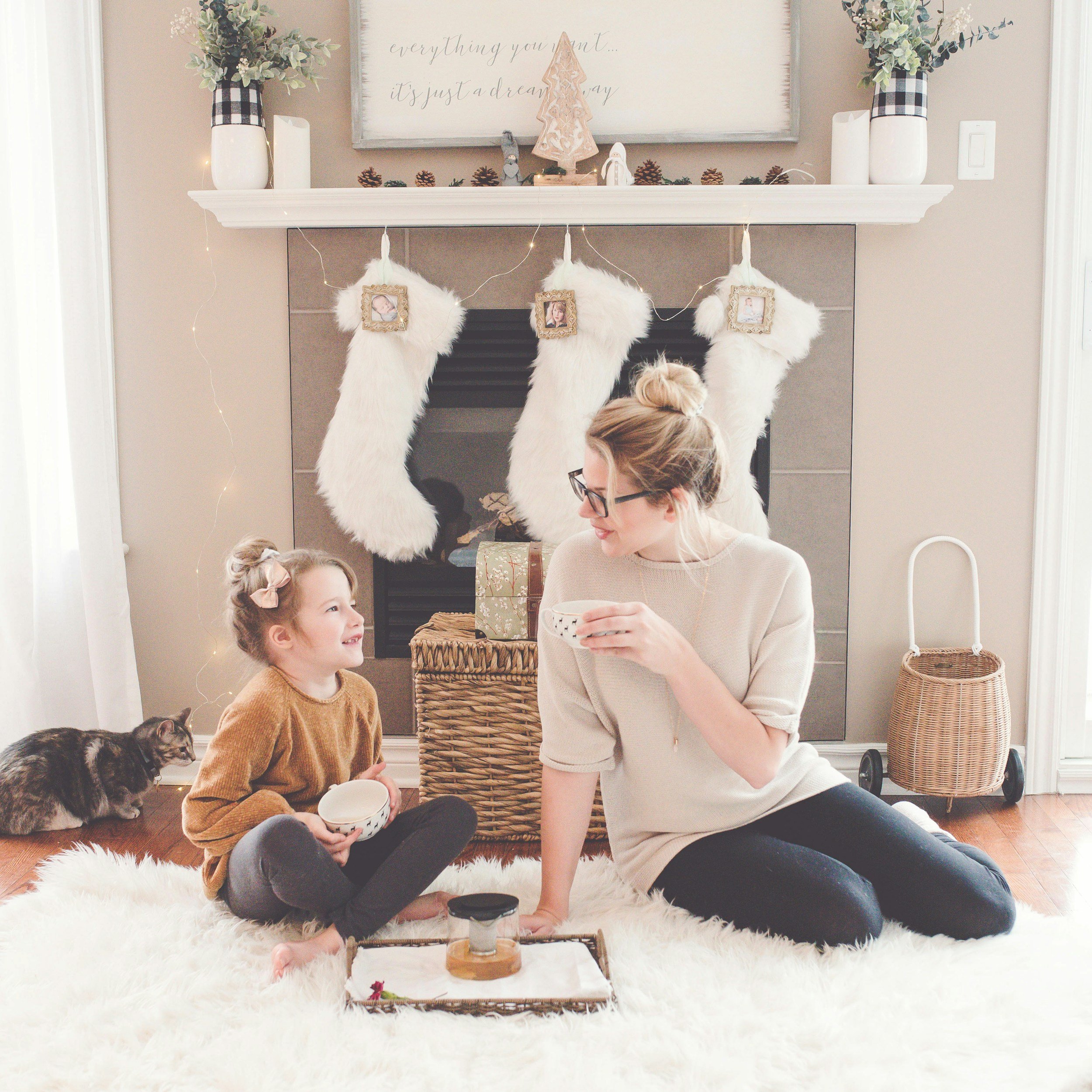 mom with a messy bun sitting on the fluffy rugh with daughter with bun, drinking tea with stockings behind them, therapy for moms fort collins, colorado