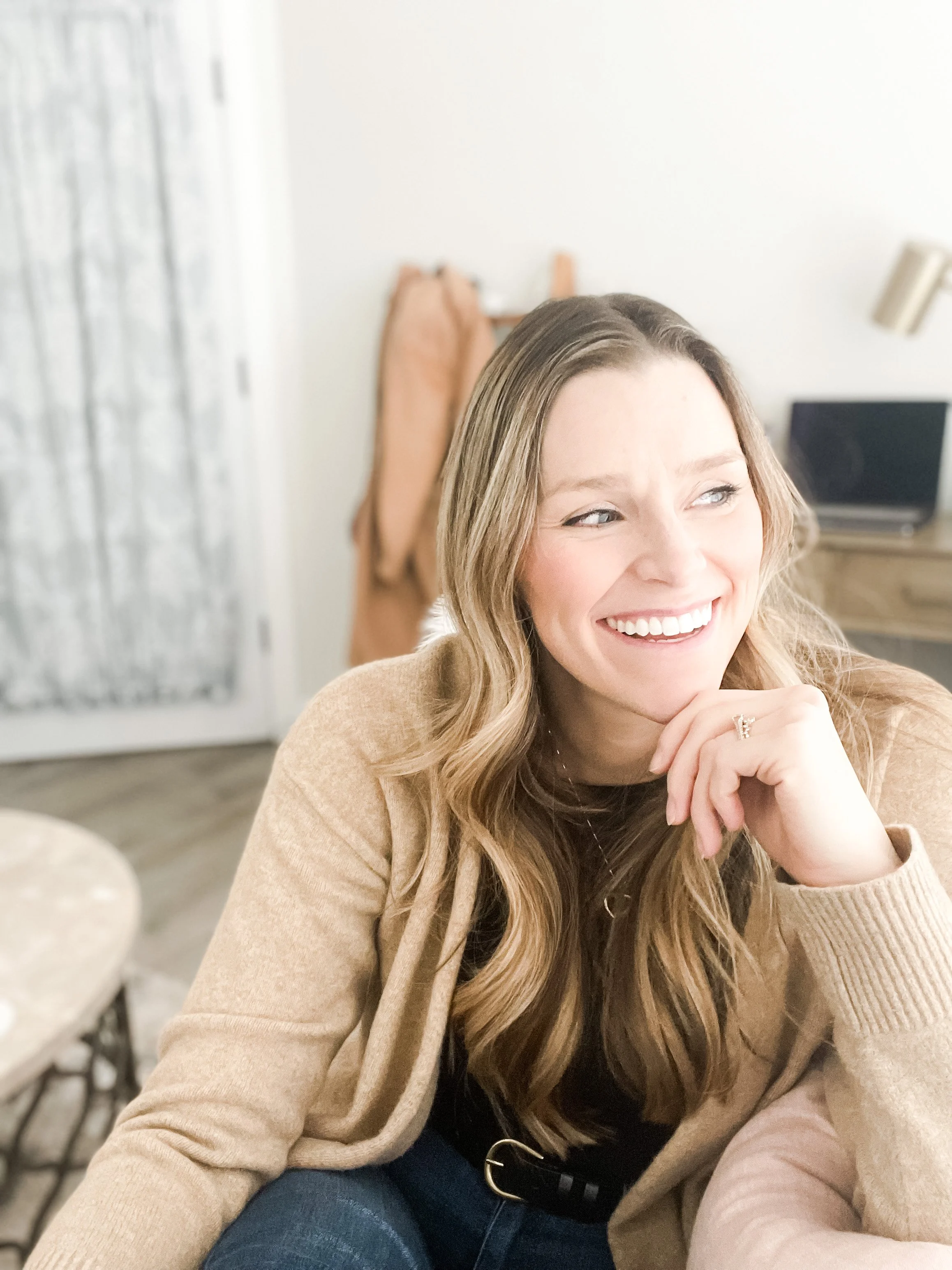 woman with long, wavy blond hair smiling in brown sweater and jeans, therapist for women and moms in fort collins