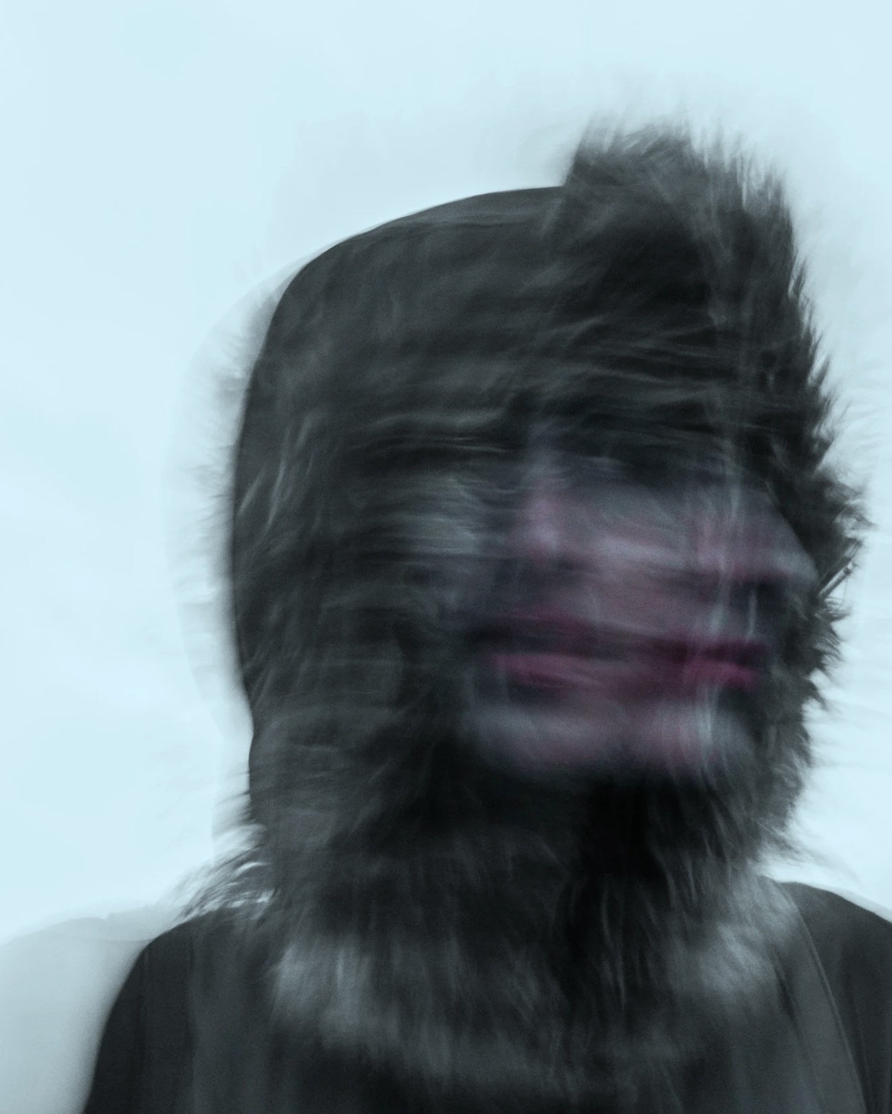 A person with long, dark hair and a beard, blurred in motion against a plain white background.