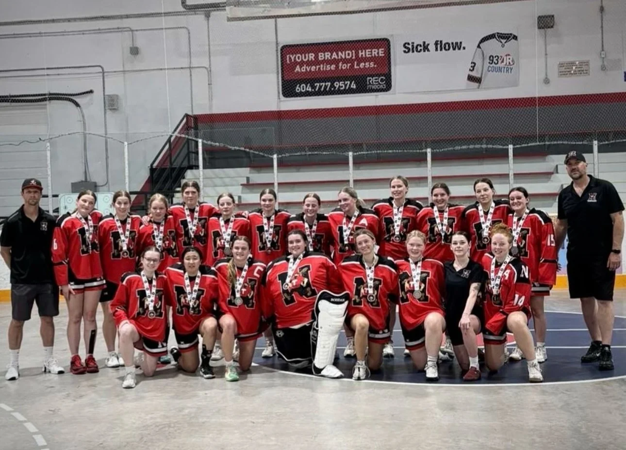 A women's hockey team in red and black jerseys celebrating with medals on an ice rink.