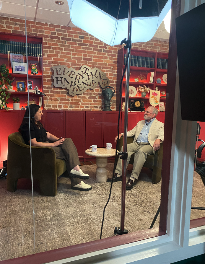 Two people recording an interview in a library studio with an umbrella light and cameras